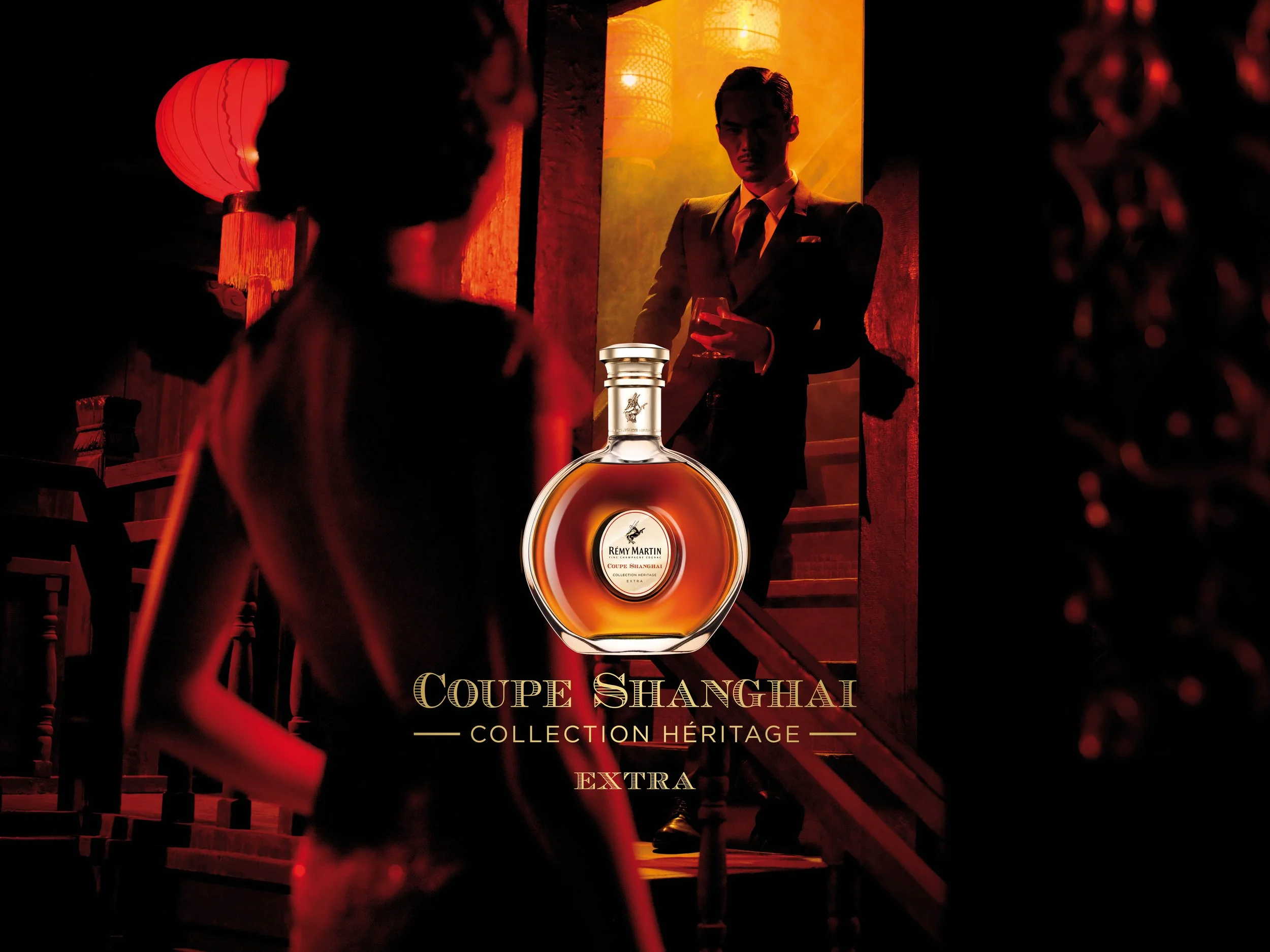 Remy Martin Coupe Shanghaï Une publicité pour le cognac Rémy Martin Coupé Shanghai, Collection Héritage, Extra, avec un flacon placé devant une scène élégante où un homme en costume et une femme en robe se trouvent dans un lieu sombre et sophistiqué.