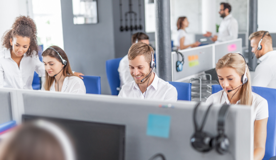 Call center agents working at their desks with headsets and computers, smiling and assisting customers.