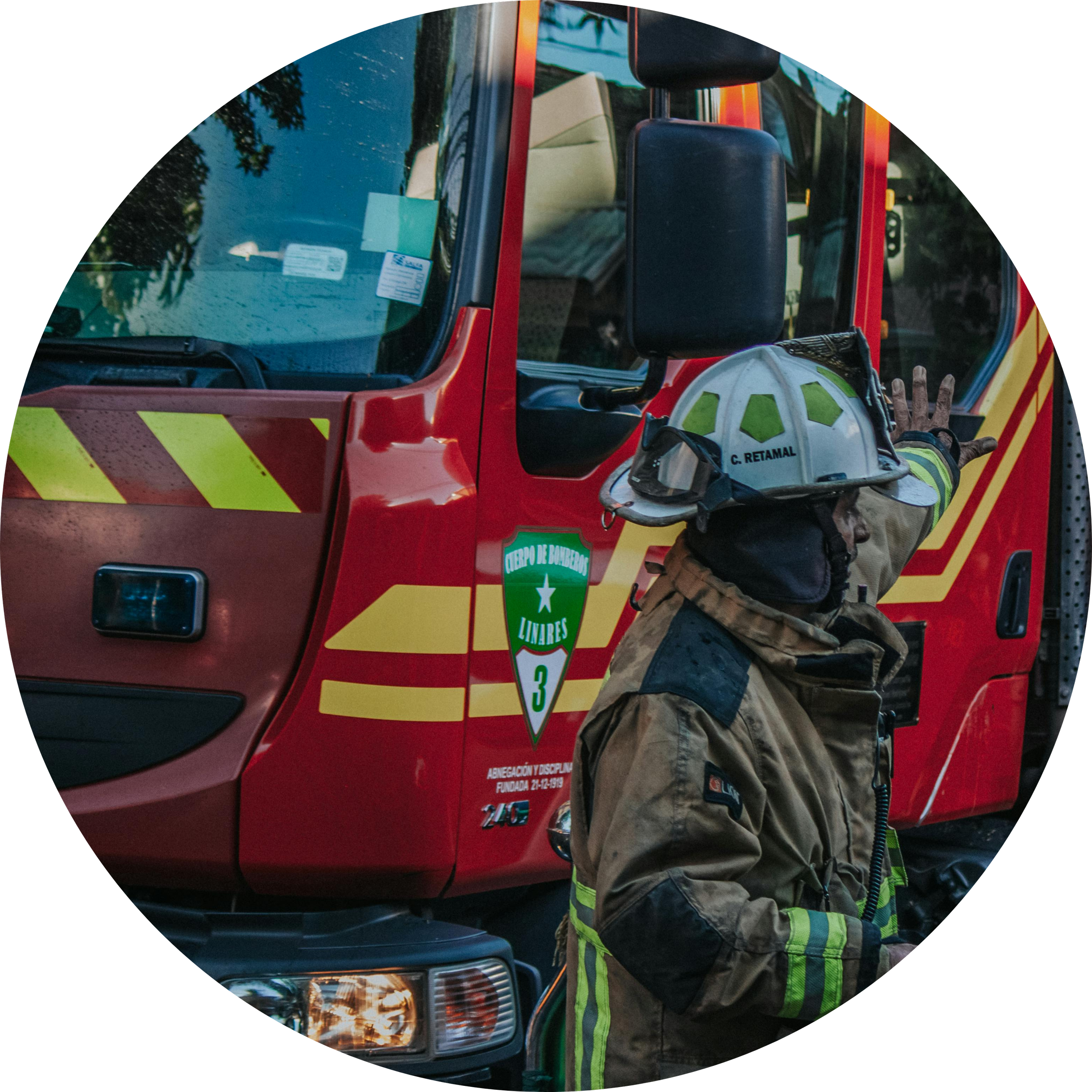 A firefighter in protective gear and helmet standing next to a red fire truck with a green and white emblem.