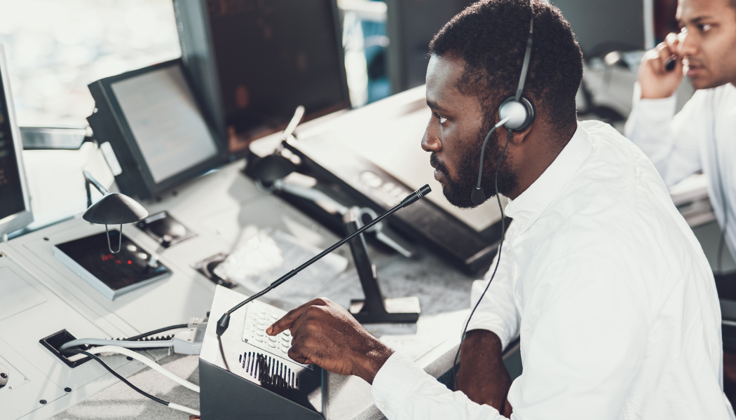 A man wearing a headset and white shirt working at a control panel in an office environment.
