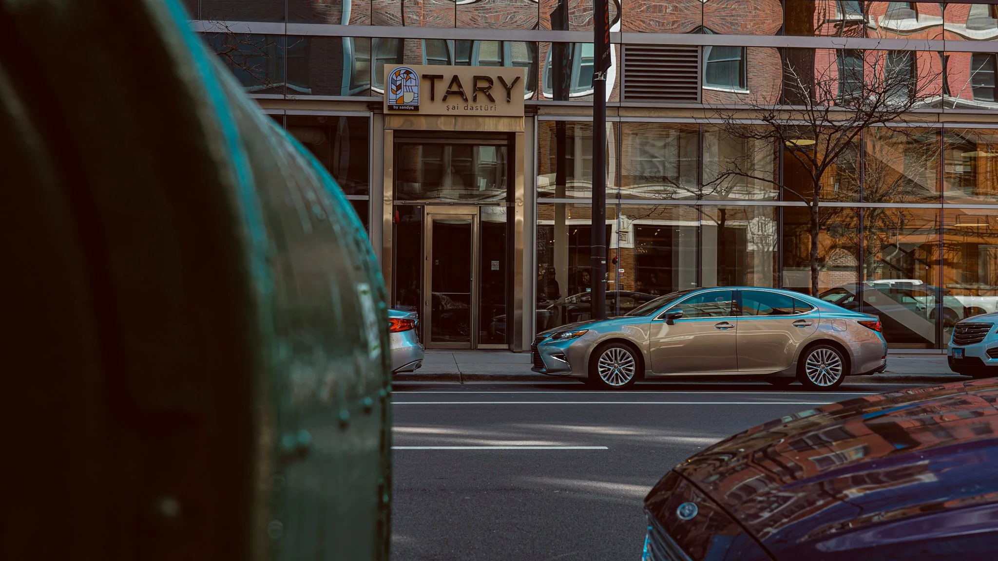 City street with parked cars and a modern restaurant with a sign reading "TARY" in the background.