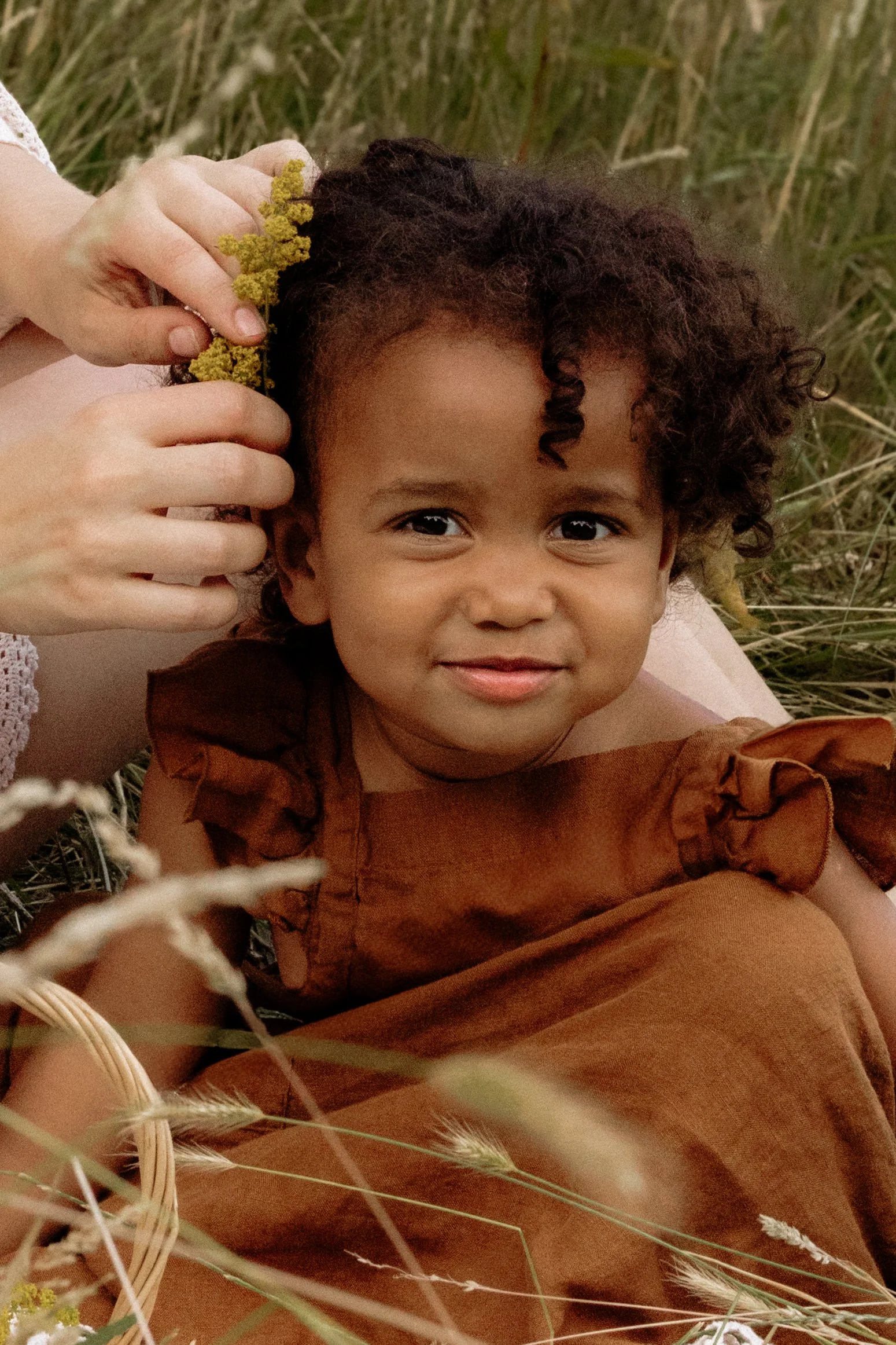 Family Photographer takes a photo of a girl in a meadow with flowers in her hair.