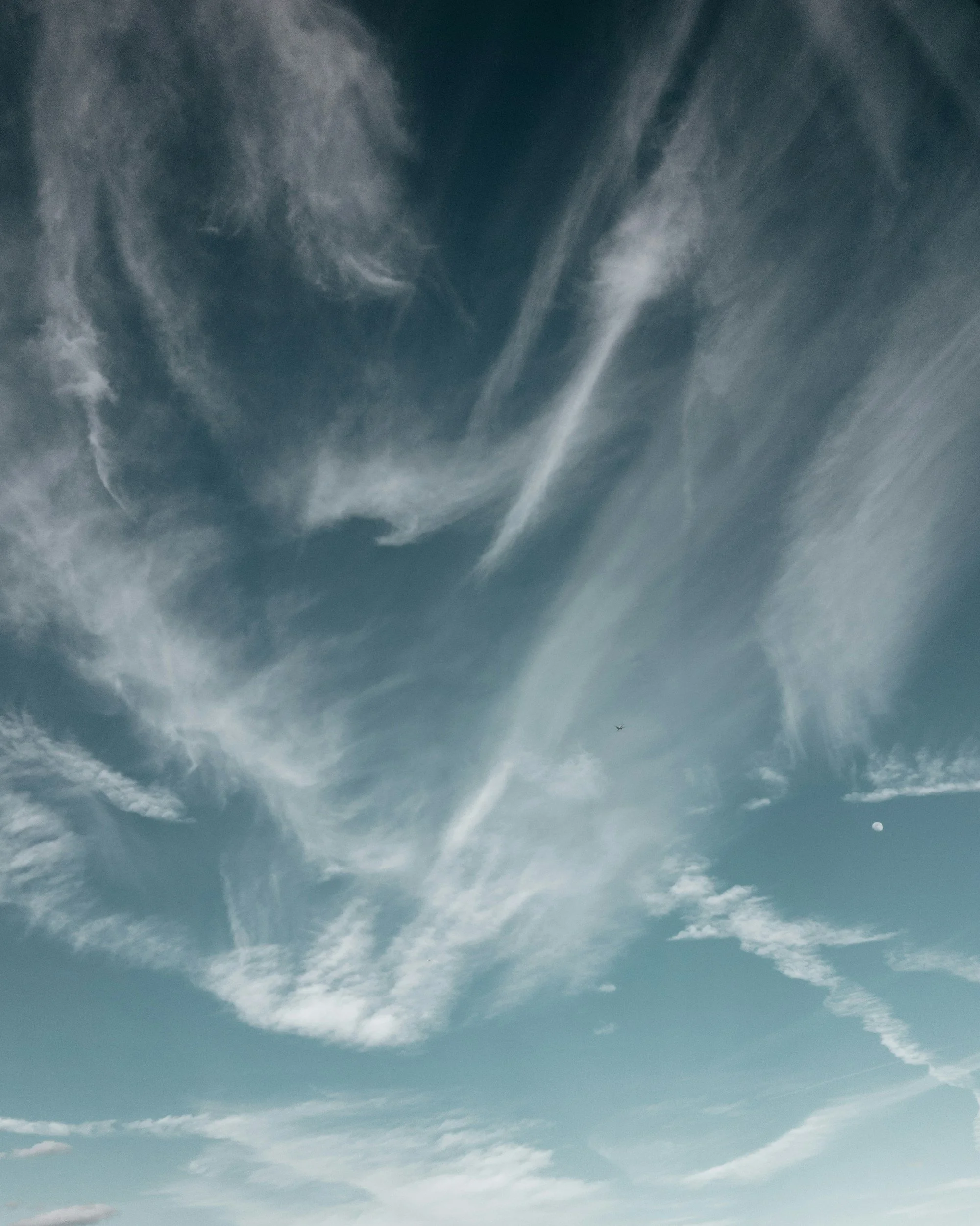 Clouds in the sky with streaks and wisps, and the moon visible in the lower right