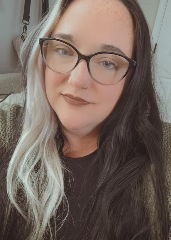 A woman with half black and half blonde hair wearing glasses, a nose ring, and a black shirt.