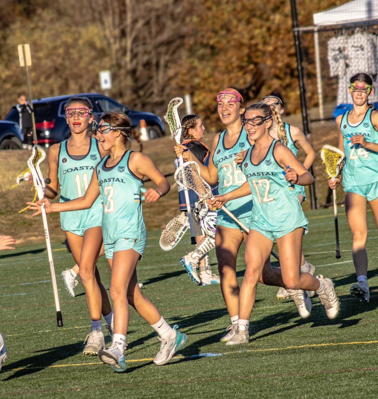 Sports photography Baltimore Maryland DMV. A group of young female lacrosse players celebrating on a field, wearing matching teal uniforms with 