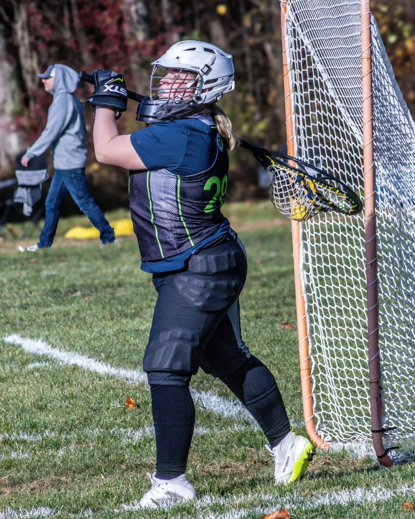 Sports photography Baltimore Maryland DMV. Lacrosse goalie in black and blue uniform with helmet and gloves preparing to block a shot near the goal on a grassy field.