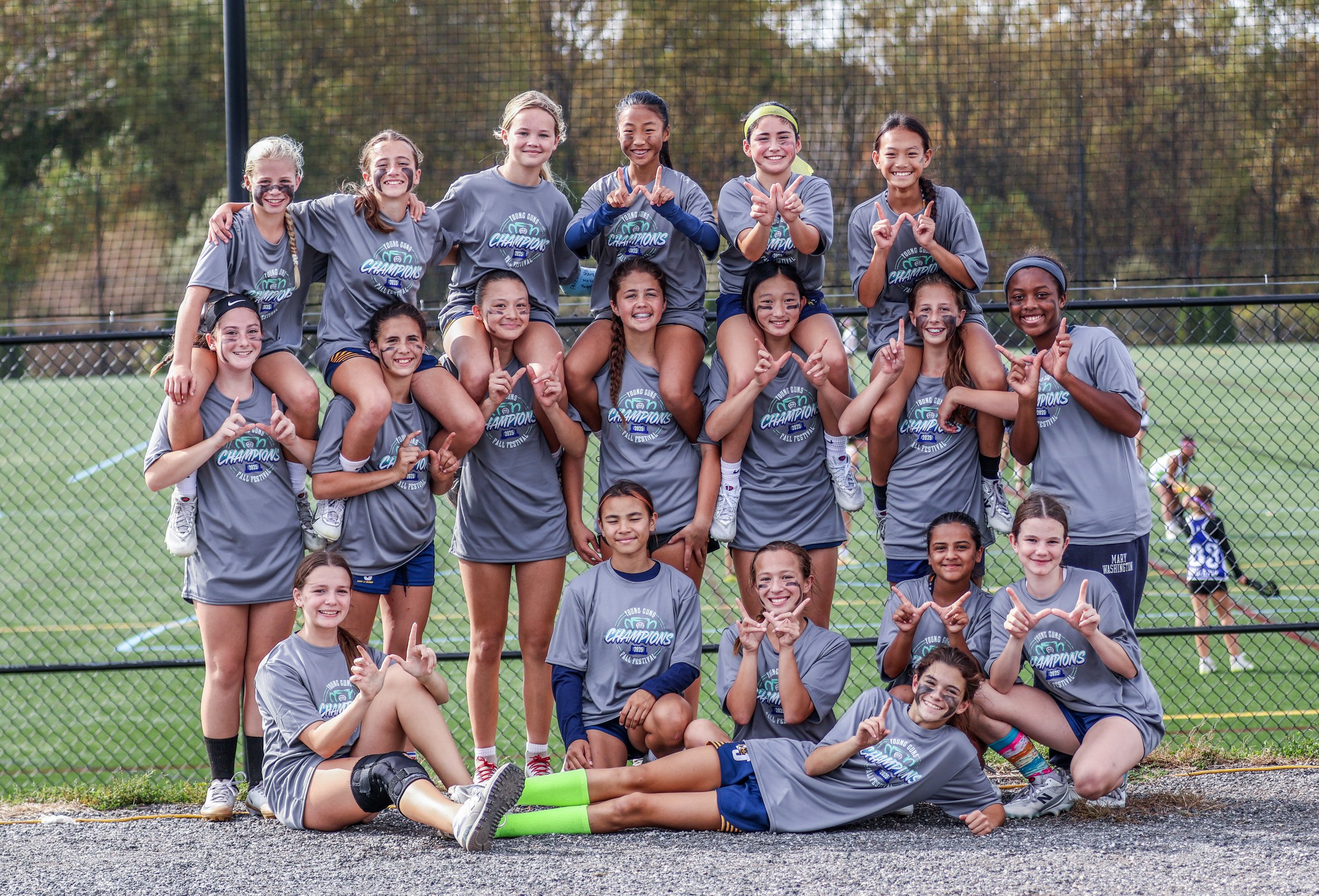 Sports photography Baltimore Maryland DMV. A group of young girls in athletic uniforms celebrating after a sports game on a field, with trees in the background.
