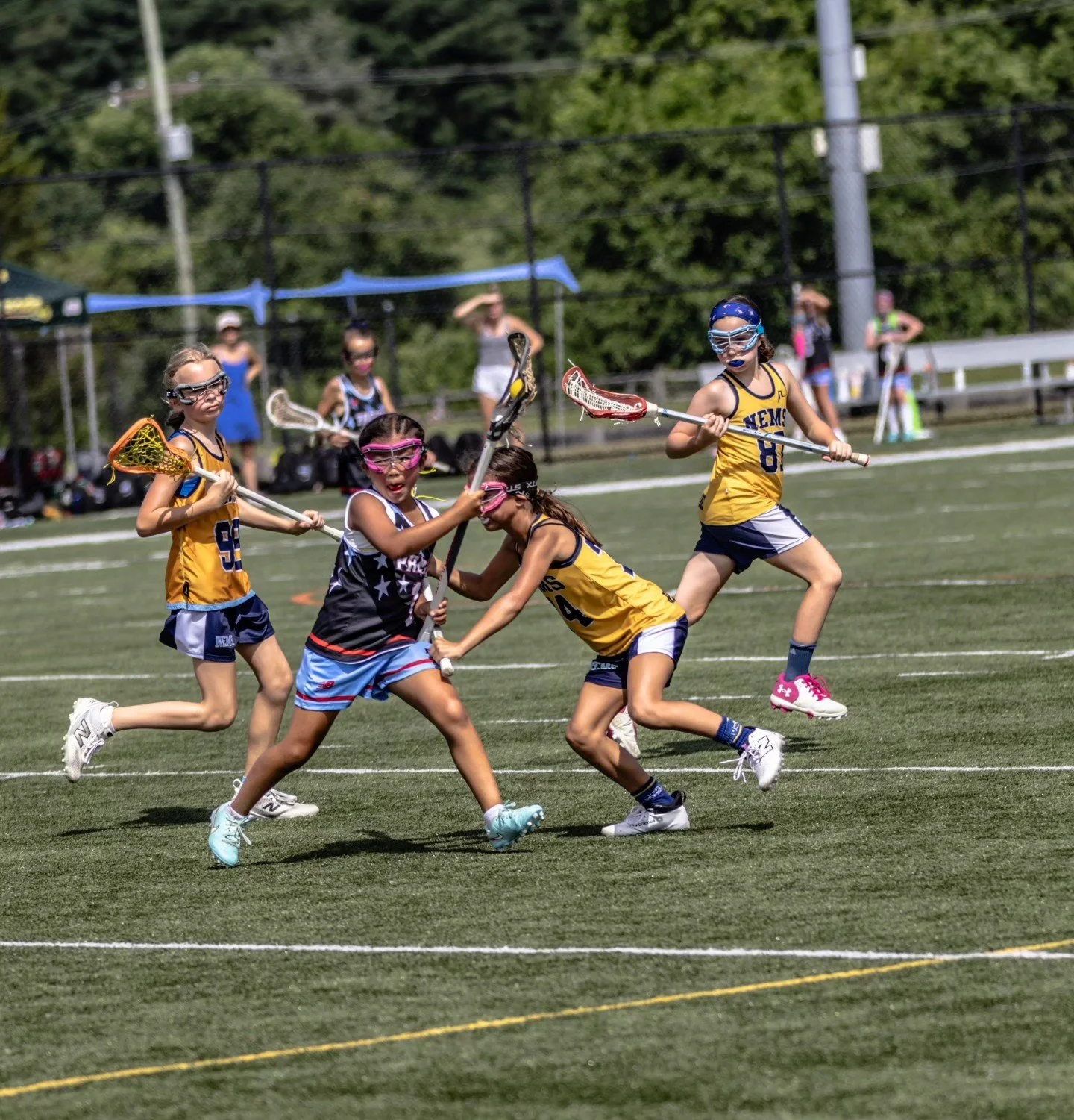 Sports photography Baltimore Maryland DMV. Children playing lacrosse on a grassy field during a sunny day, with both teams wearing colorful uniforms and goggles.
