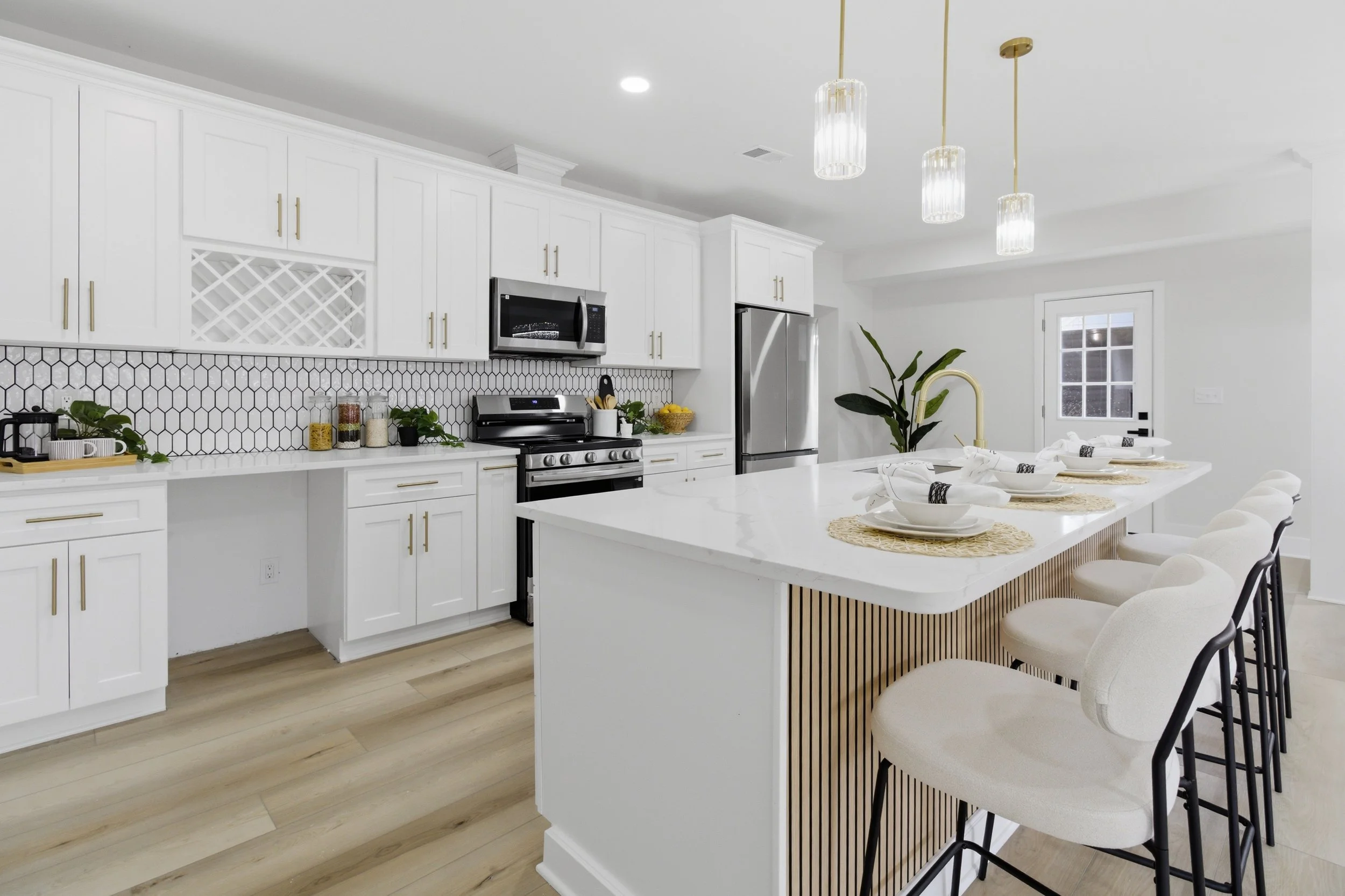 Modern white kitchen with a large island, built-in cabinets, stainless steel appliances, barstools, and pendant lighting.