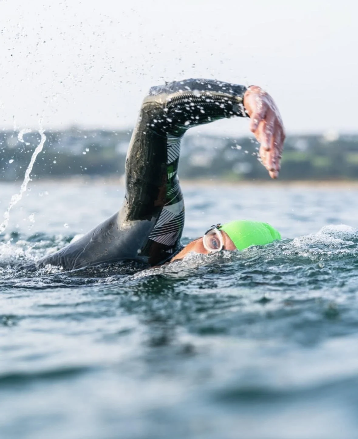 Swimmer in a wetsuit and green swim cap practicing open water swimming with a pink fish