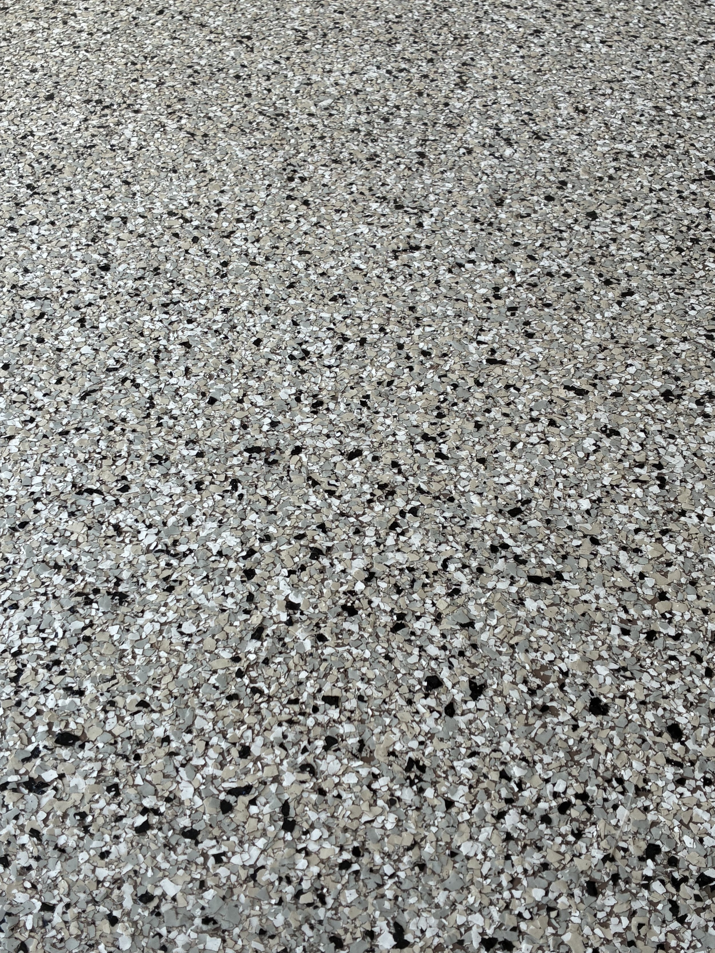 Close-up of a speckled epoxy floor with beige, black, gray, and white chips.