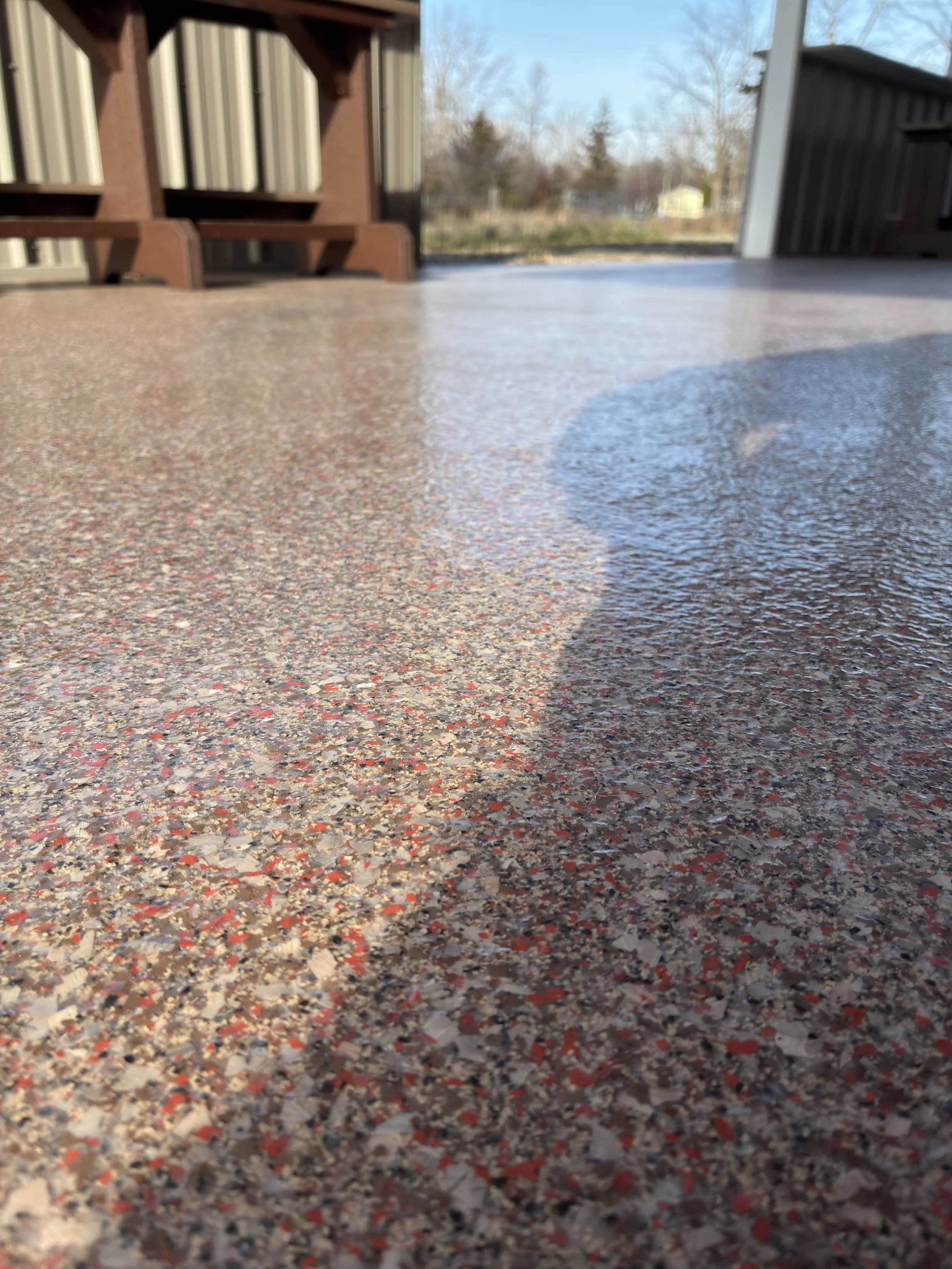 Close-up of a textured outdoor concrete surface with wet patch, brown wooden structures, and a background of trees and sky.