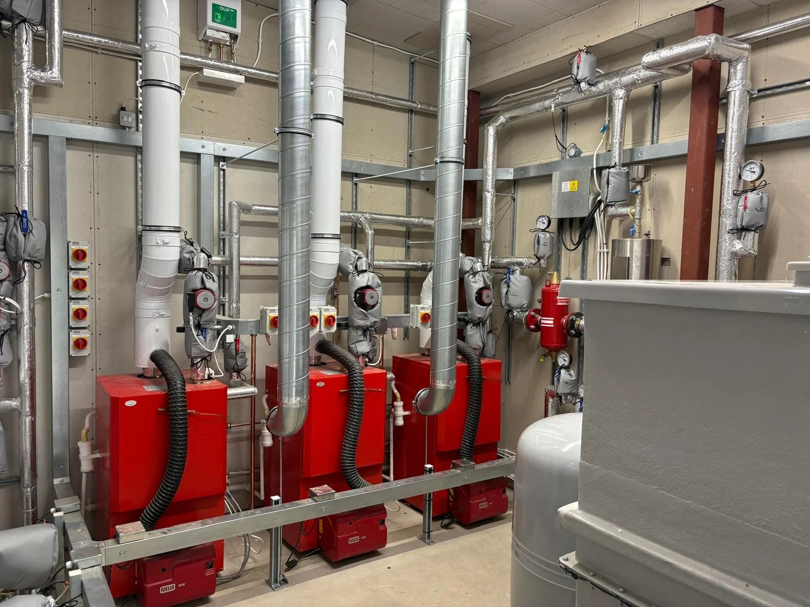 Industrial HVAC room with red units, insulated ducts, gauges, valves, and control panels.