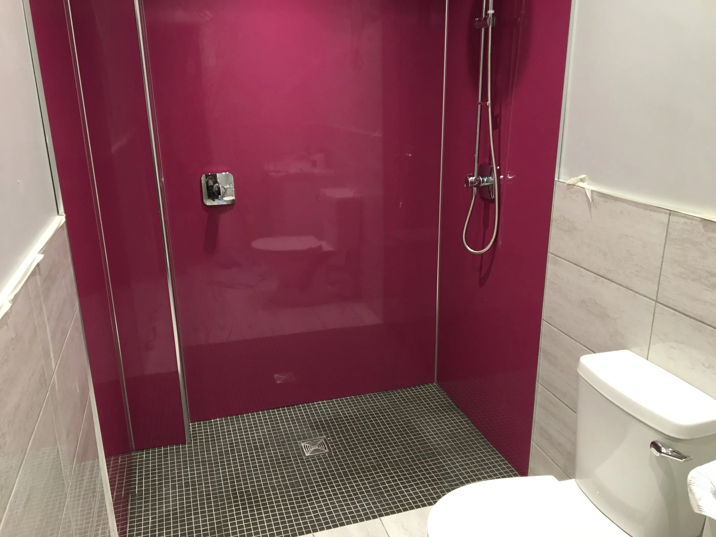 Modern bathroom with a magenta shower enclosure, black tiled floor, and a white toilet.