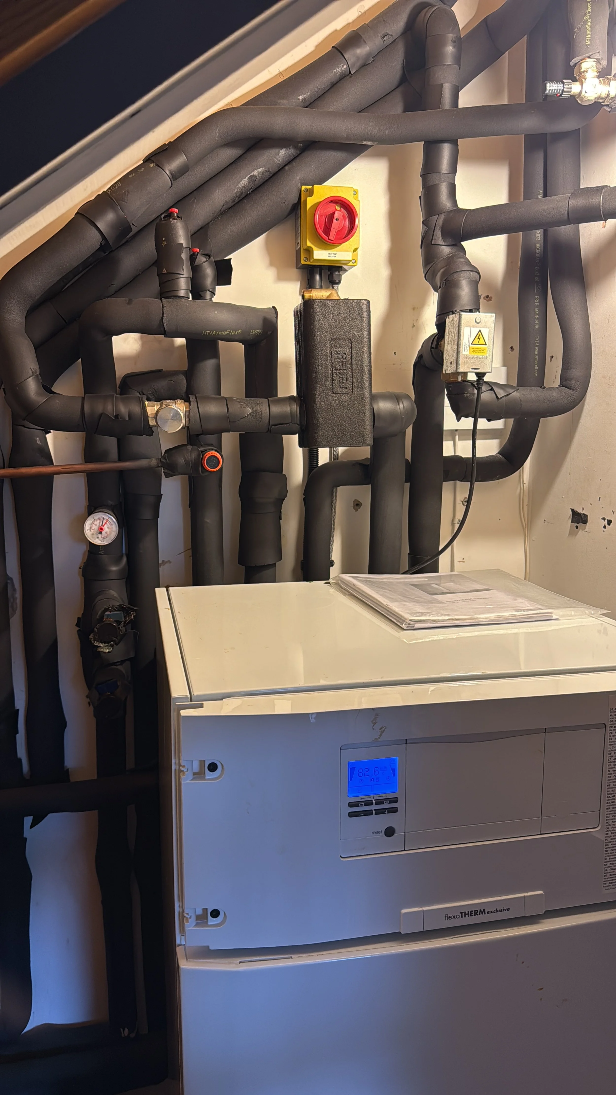 Pipes and a boiler in a mechanical room with a control panel displaying 82.6 degrees.