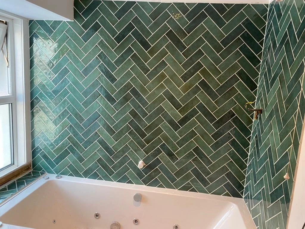Bathroom with green herringbone tile walls and a white bathtub.