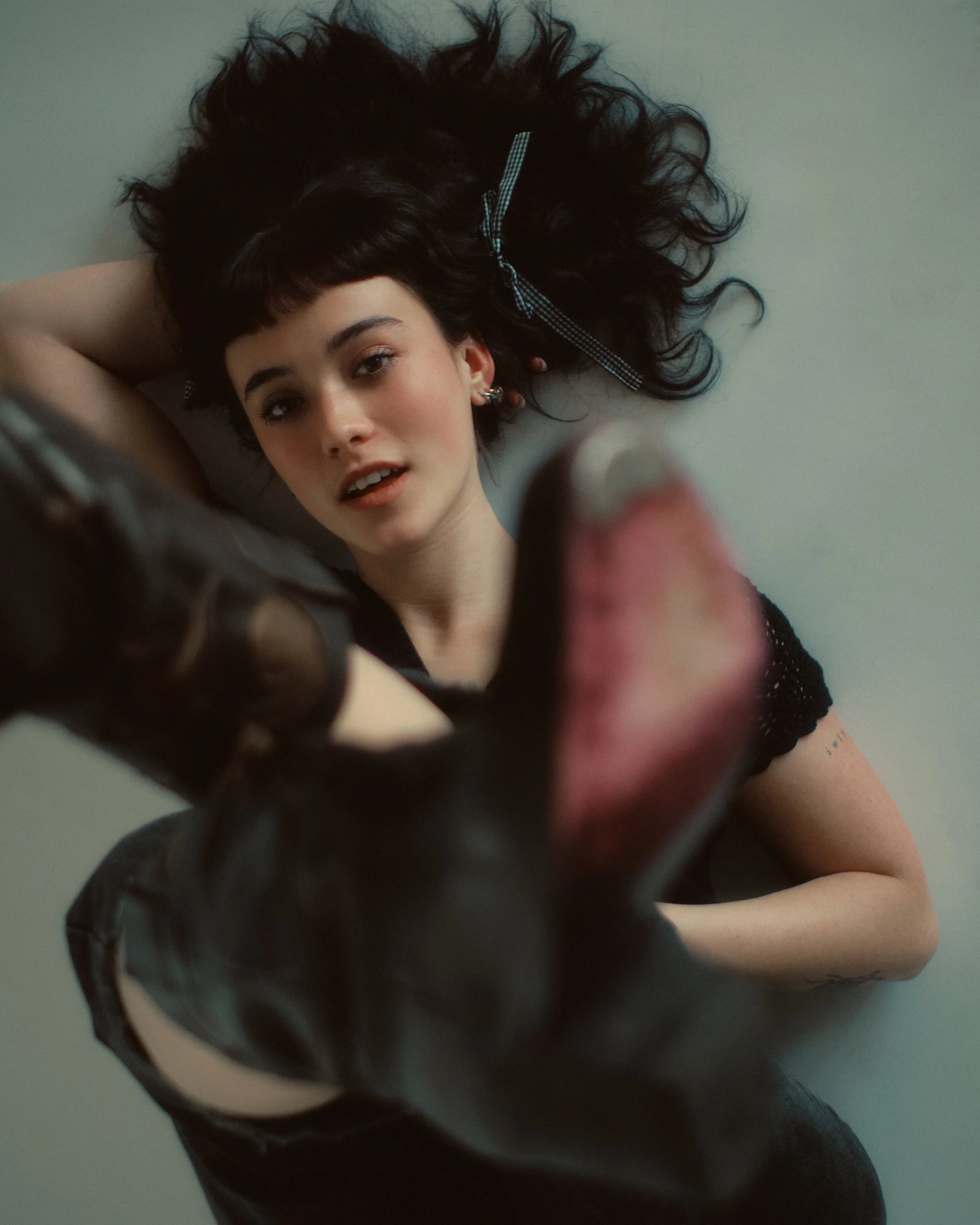 A young woman with dark curly hair lying on her back pulling her tongue out towards the camera.