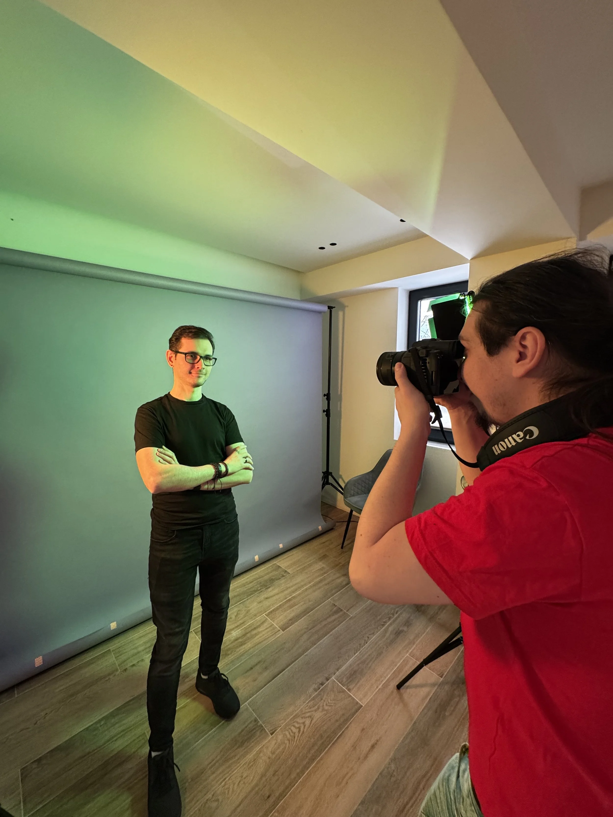 Person taking a photo of a model in a studio with a colored backdrop.
