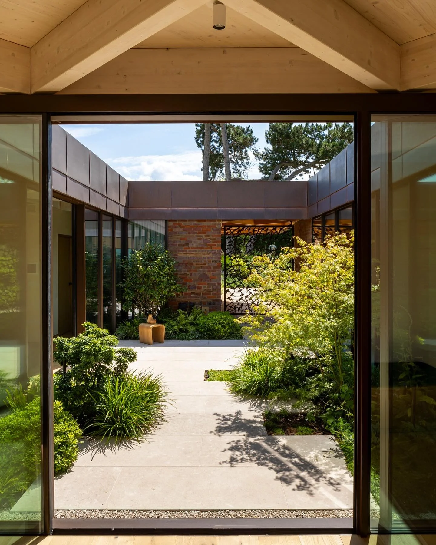 View of a modern indoor-outdoor area with large glass sliding doors opening to a courtyard garden with lush greenery and a paved walkway.