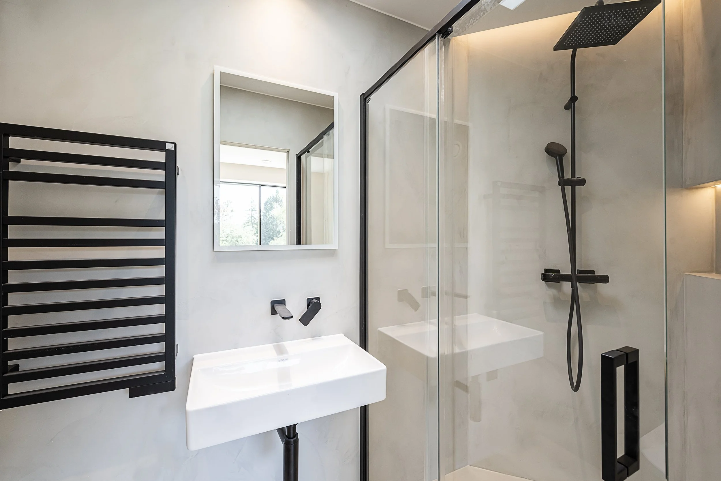 Modern bathroom with a white sink, black wall-mounted towel rack, mirror, and a glass-enclosed shower with black fixtures.