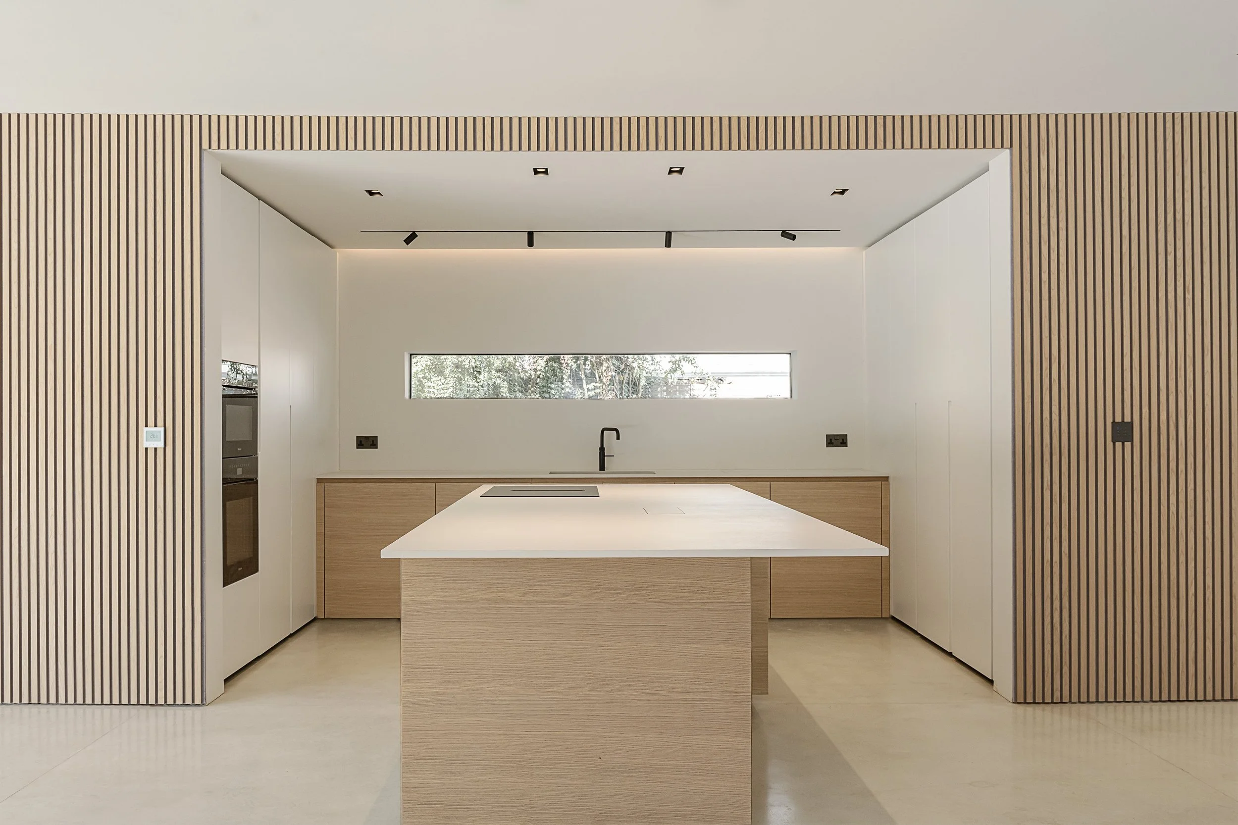 Modern kitchen with light wood cabinetry, a white island, and a horizontal window.