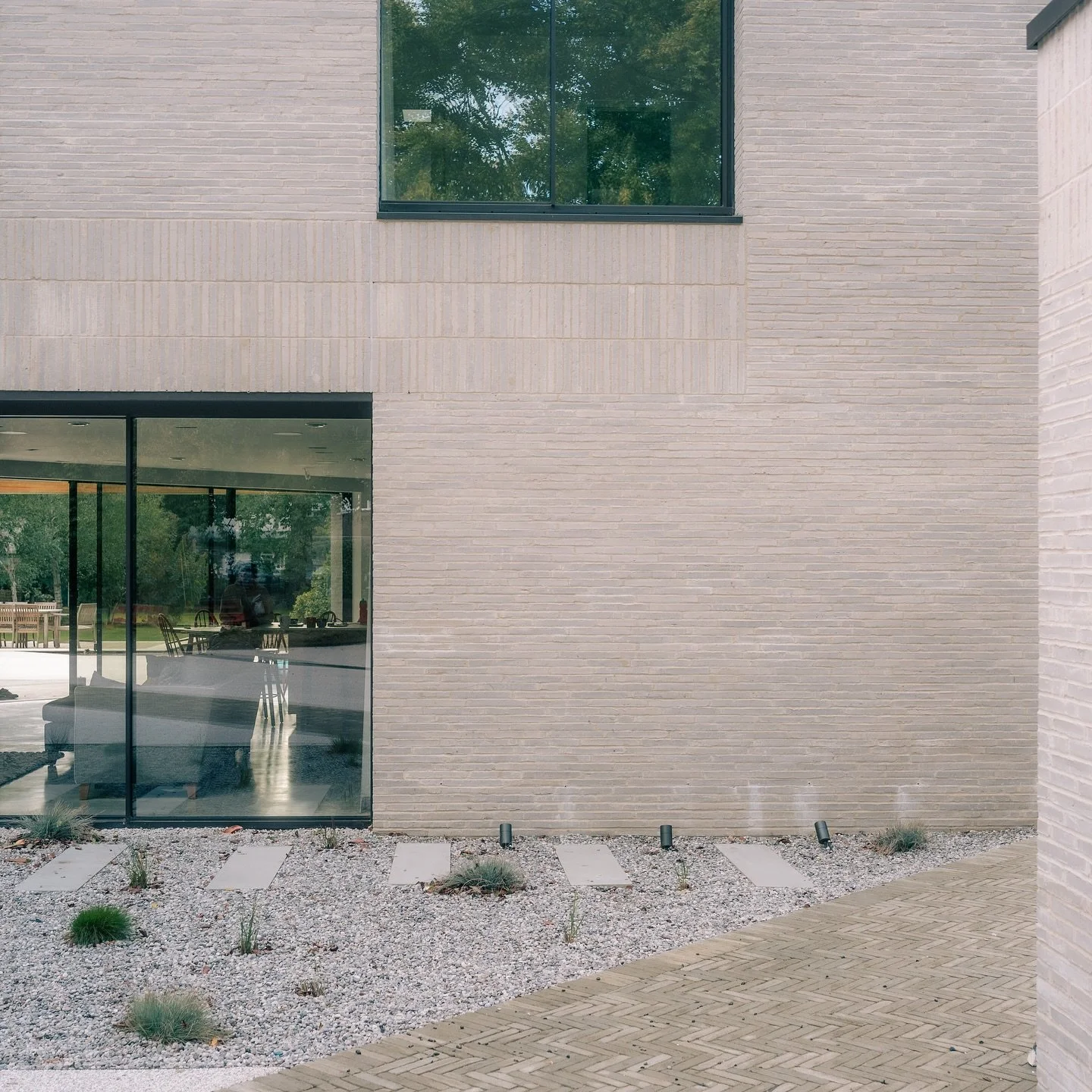 Exterior modern building with large glass windows and a minimalist landscape featuring gravel, small plants, and concrete paver stones.