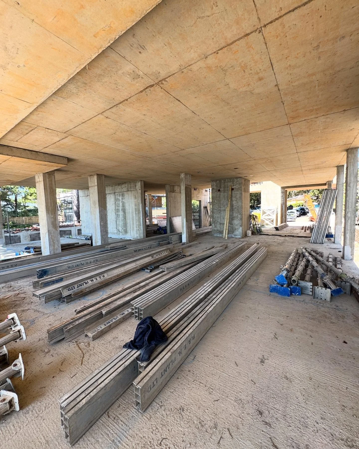 Construction site with metal beams and columns inside a partially built structure, with some construction equipment and materials scattered around.