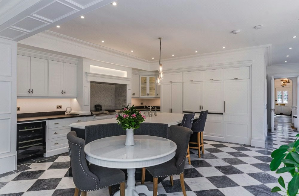 Modern kitchen with white cabinets, black countertops, checkered black and white tile floor, round dining table with flowers, and bar stools.