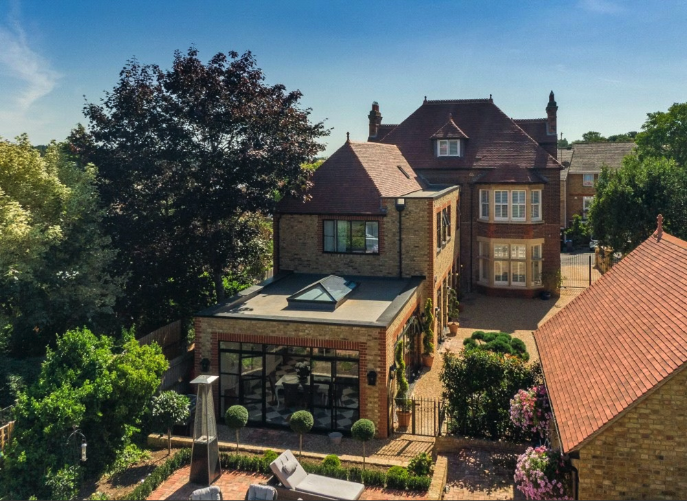A large brick house with a distinctive architectural style, surrounded by trees and a well-maintained garden."