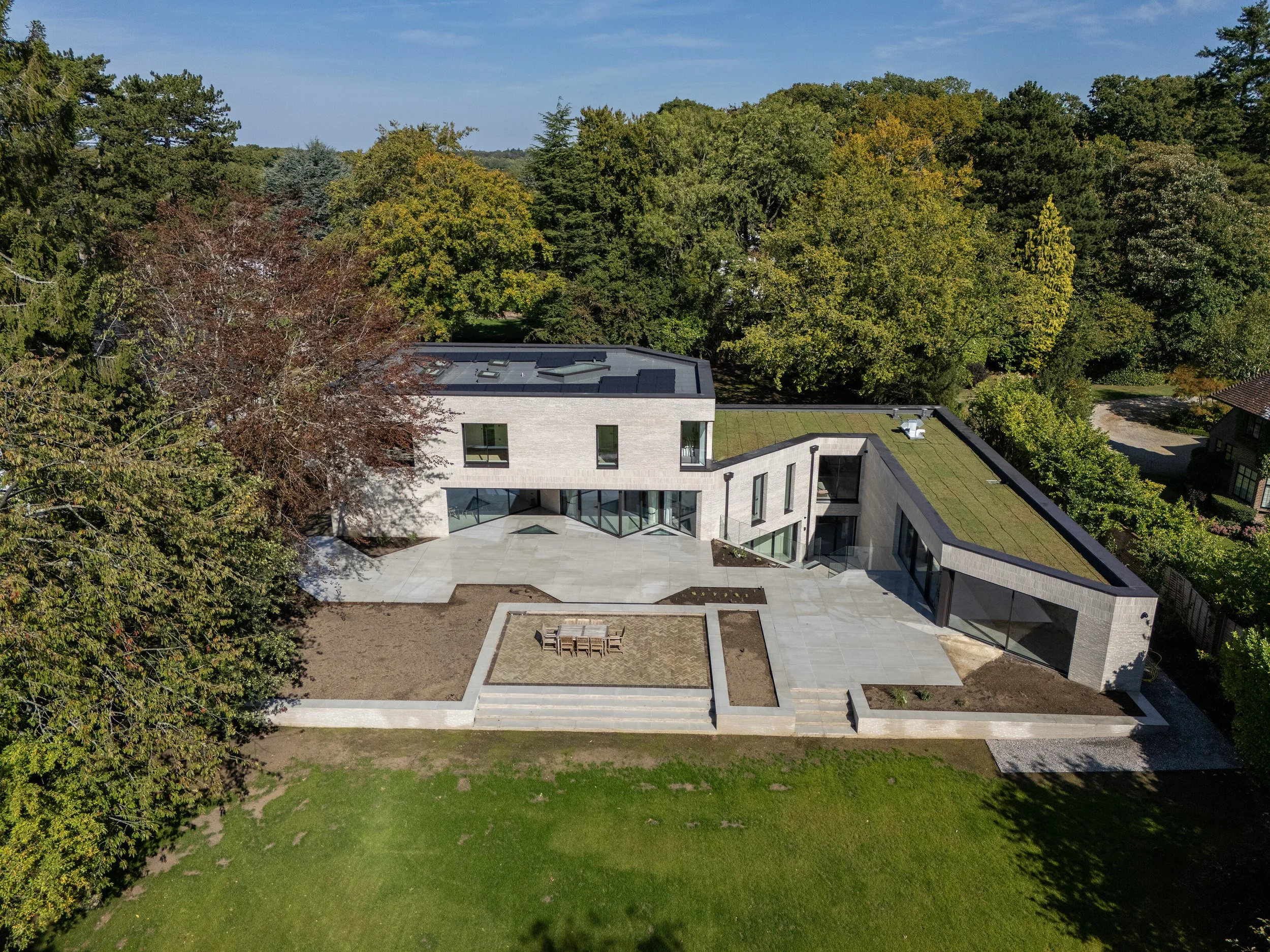Modern house with large patio, surrounded by green trees and grass yard