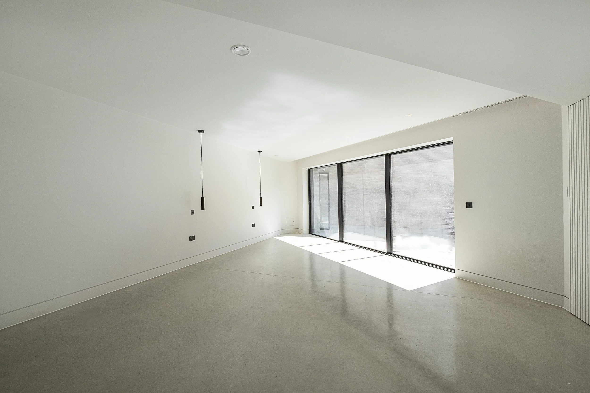 Empty modern room with large glass sliding doors, minimalistic design, white walls, and grey flooring.