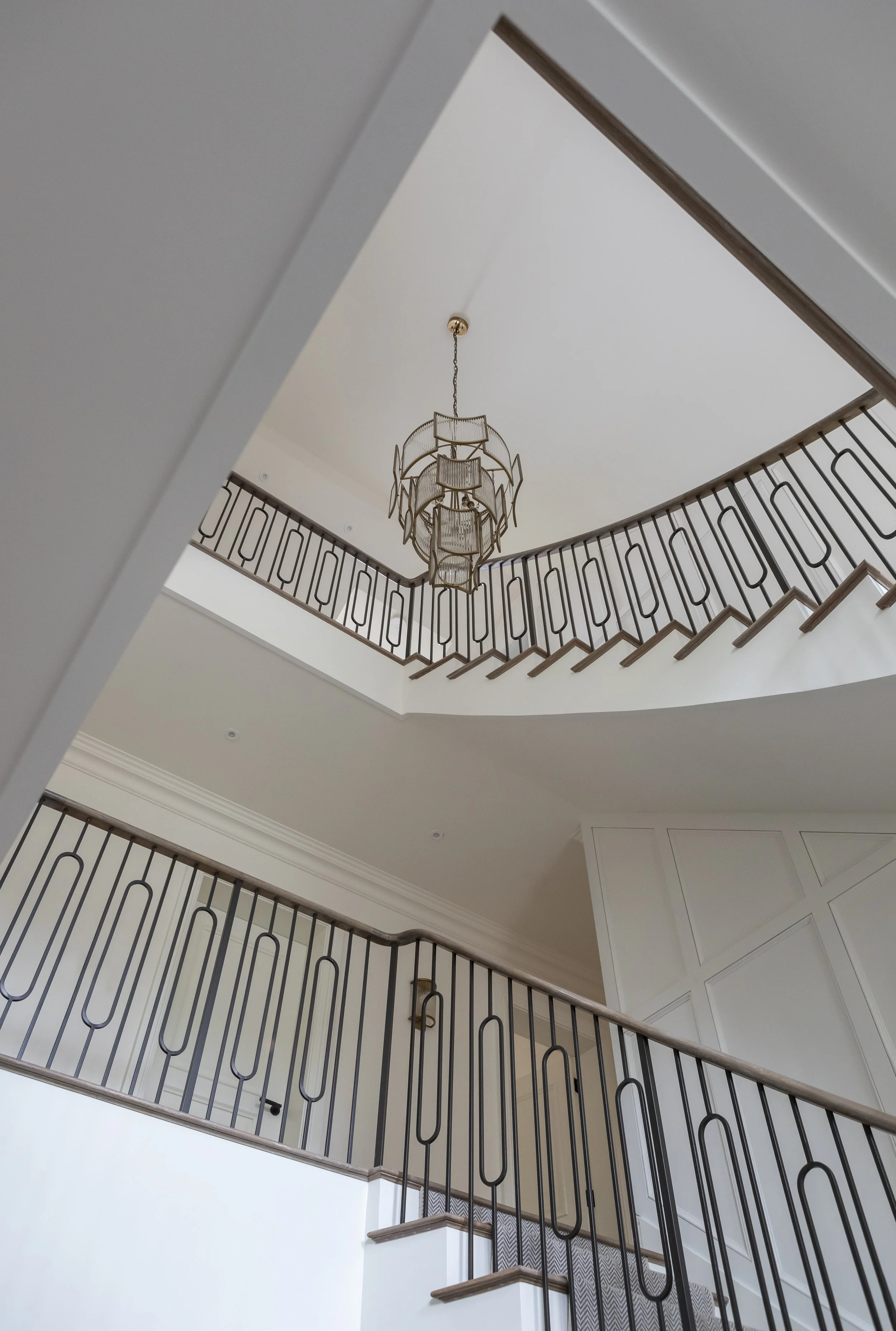 View of a multi-level staircase with metal railings, seen from below, featuring a modern chandelier hanging from the ceiling.