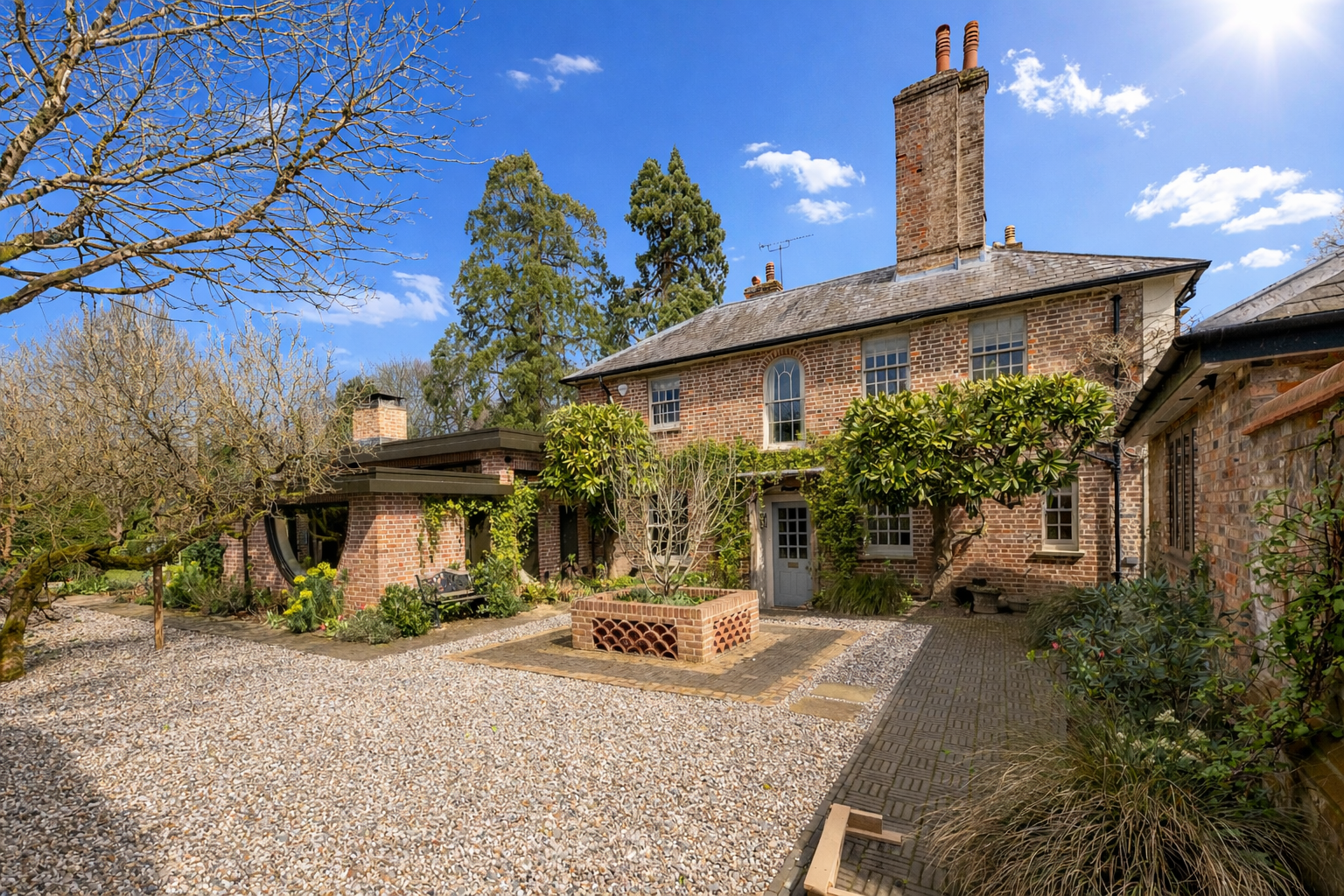 A brick house with a garden patio, trees, and a blue sky with scattered clouds.