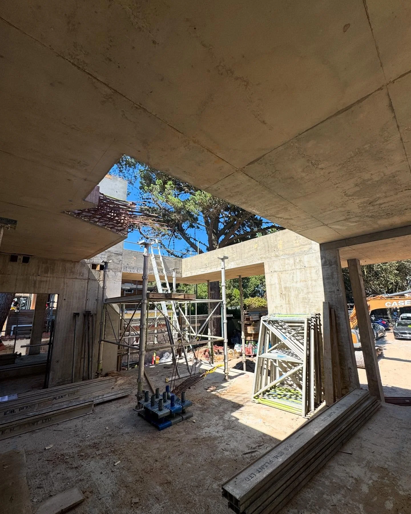 Construction site with concrete structure, scaffolding, ladders, and construction materials under a clear blue sky.
