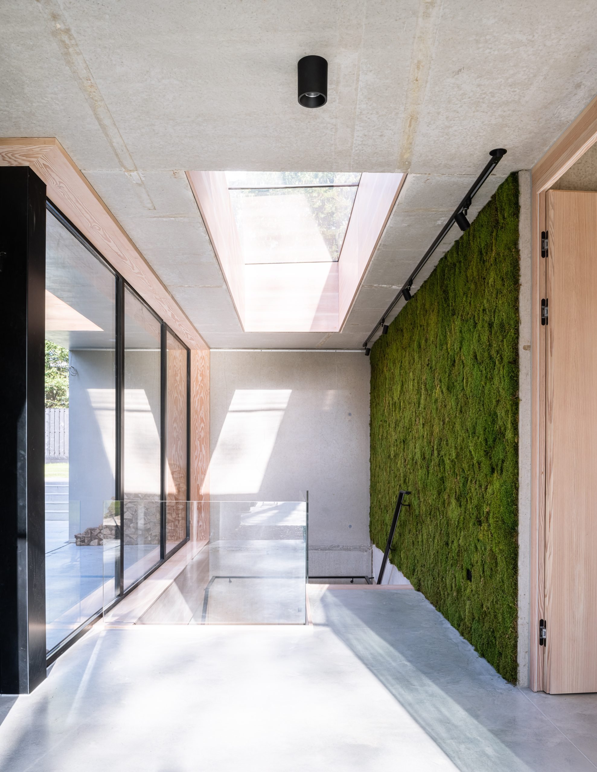 Modern interior space with concrete floors, large window, green moss wall, and ceiling skylight.