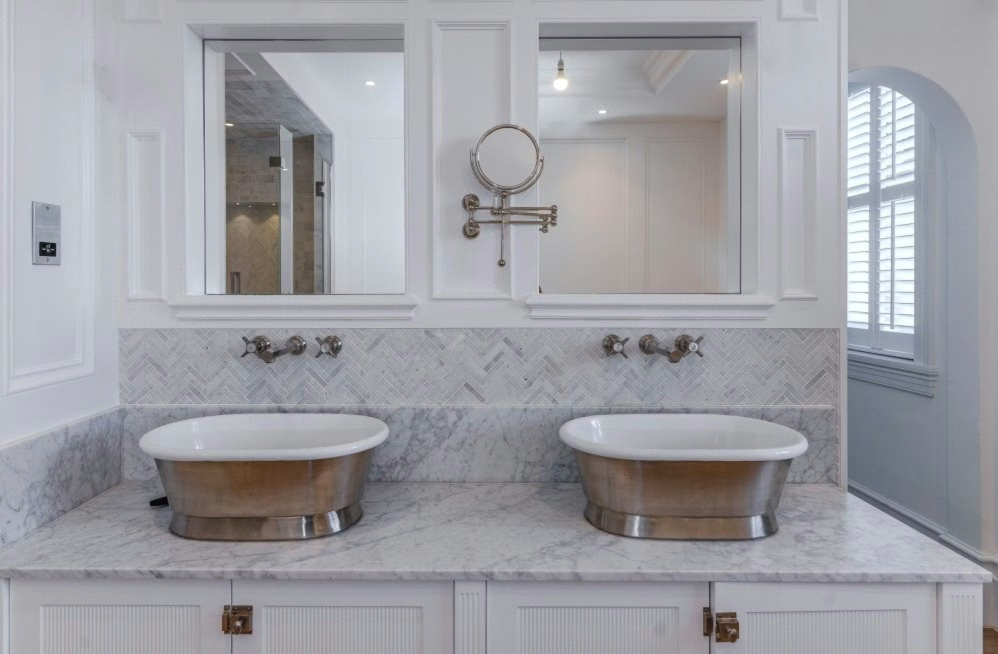 A luxurious bathroom with two bathtub sinks, marble countertops, and large mirrors.