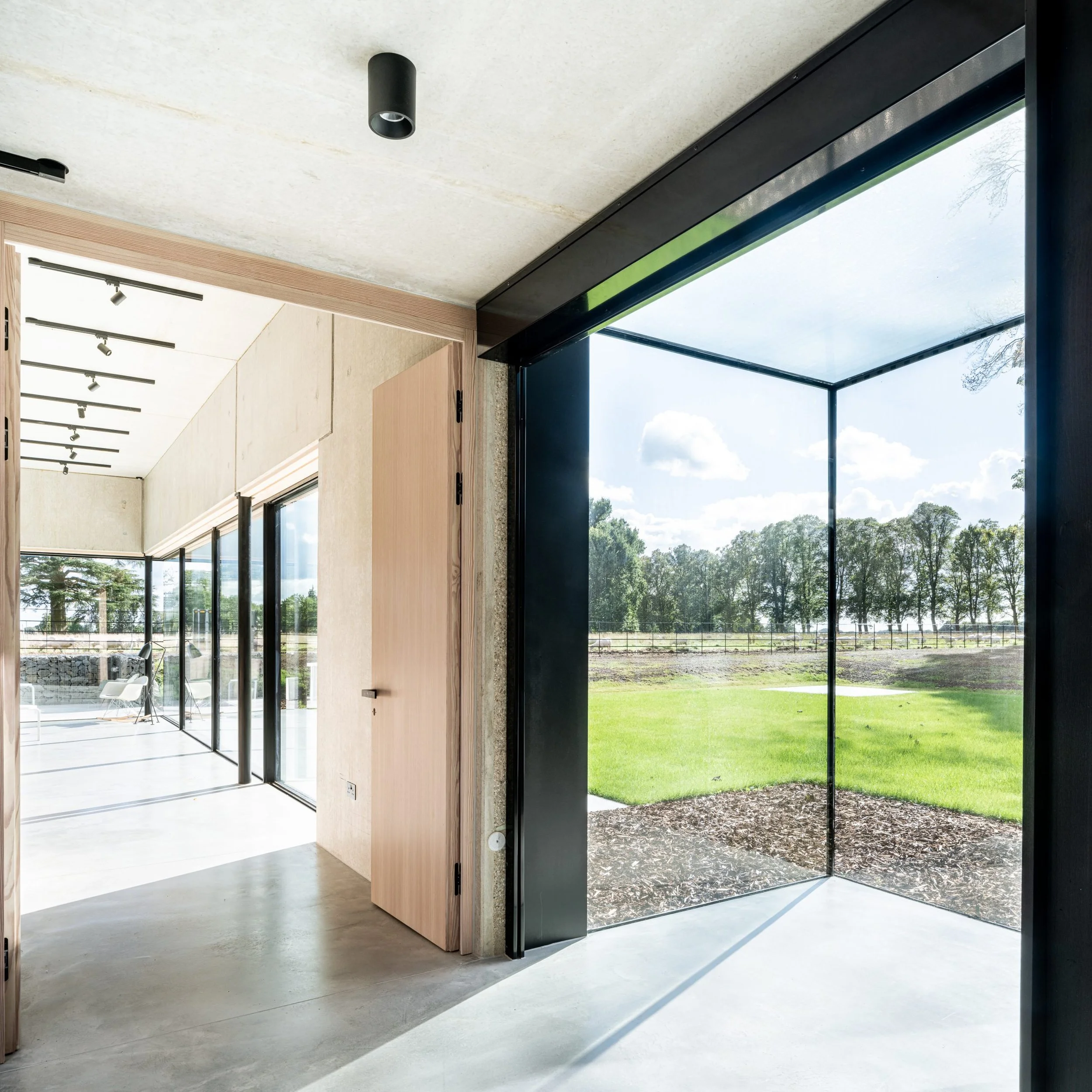 Interior space with large glass doors and windows opening to a grassy outdoor area with trees and a partly cloudy sky.