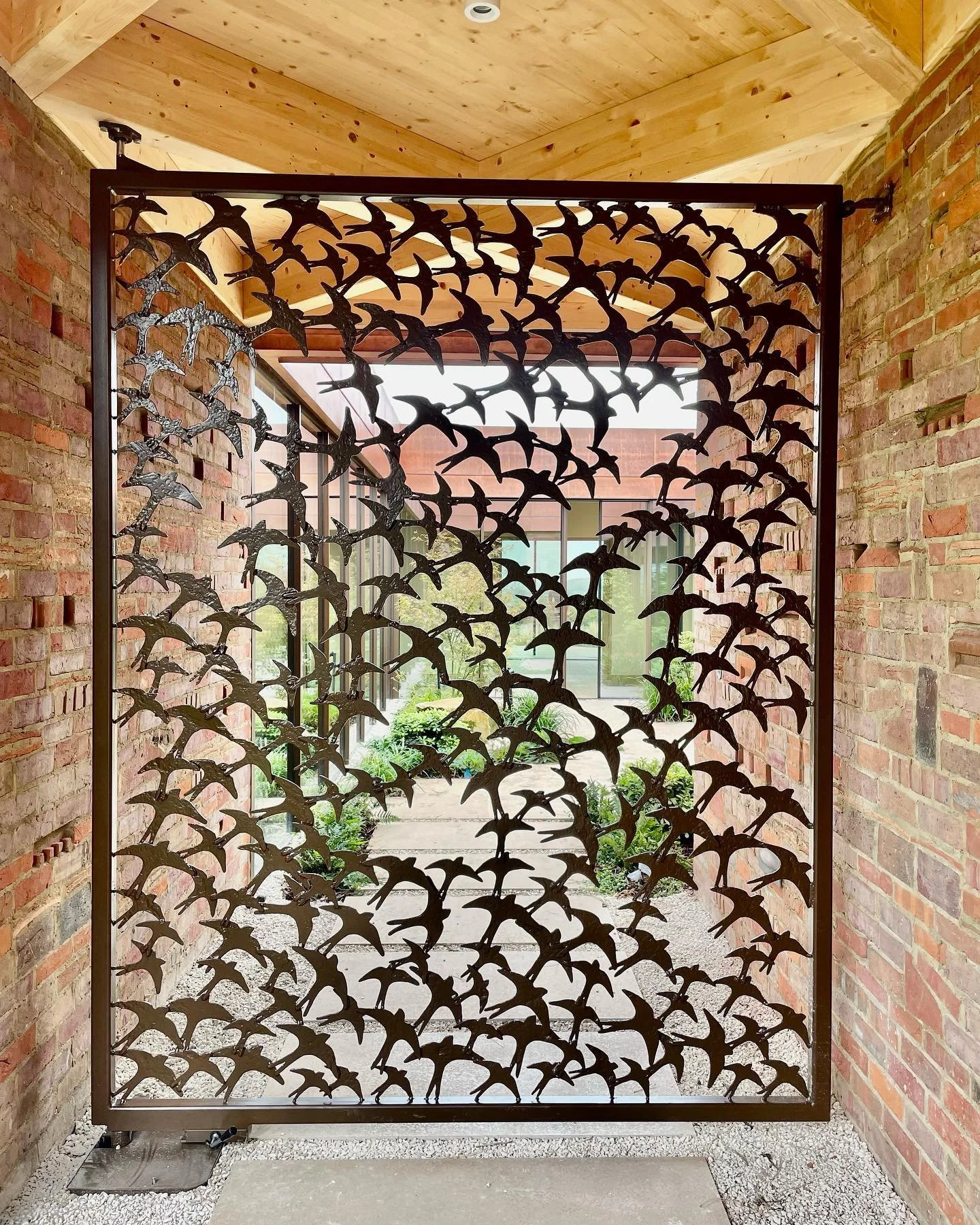 Decorative metal screen with cutout bird shapes, placed between brick walls in an indoor corridor.