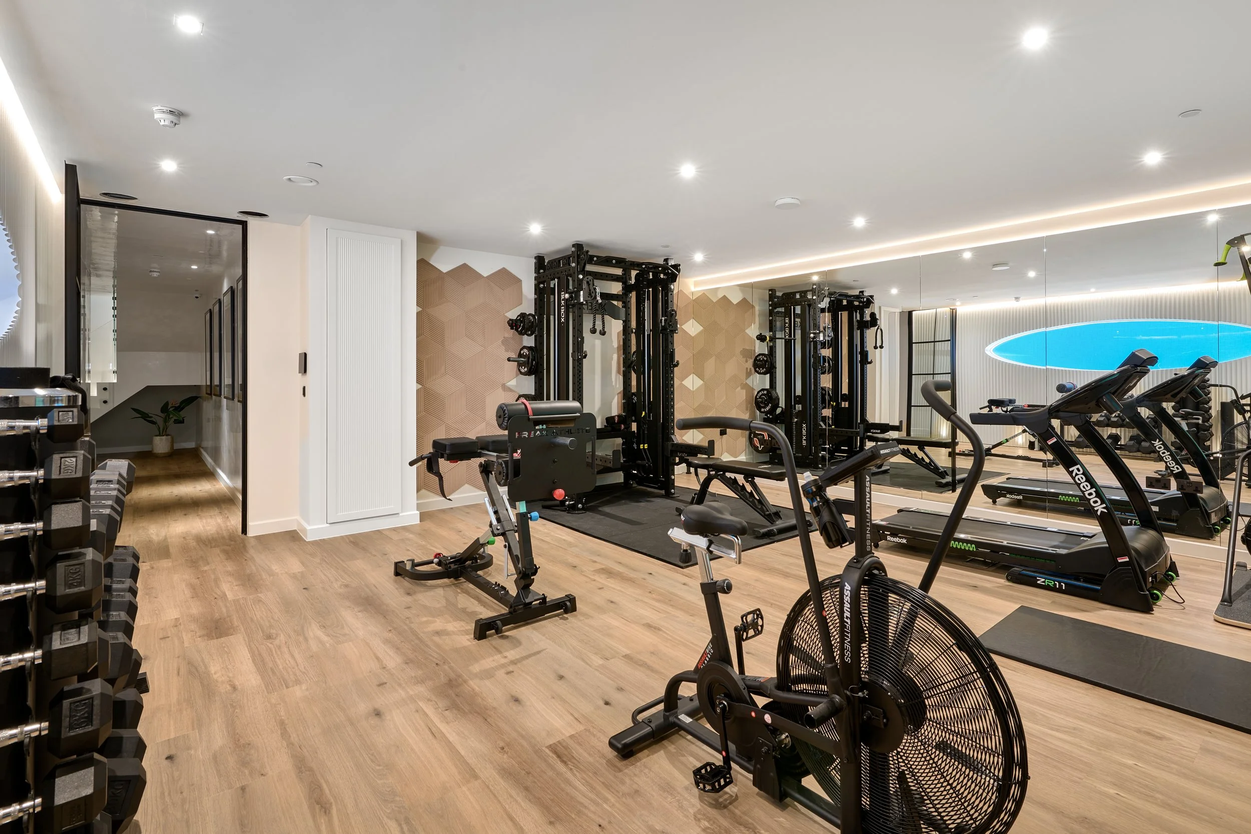 Modern home gym with various workout equipment, including a treadmill, stationary bike, free weights, and strength training machines, with wooden floors, decorative wall panels, and a large mirror.