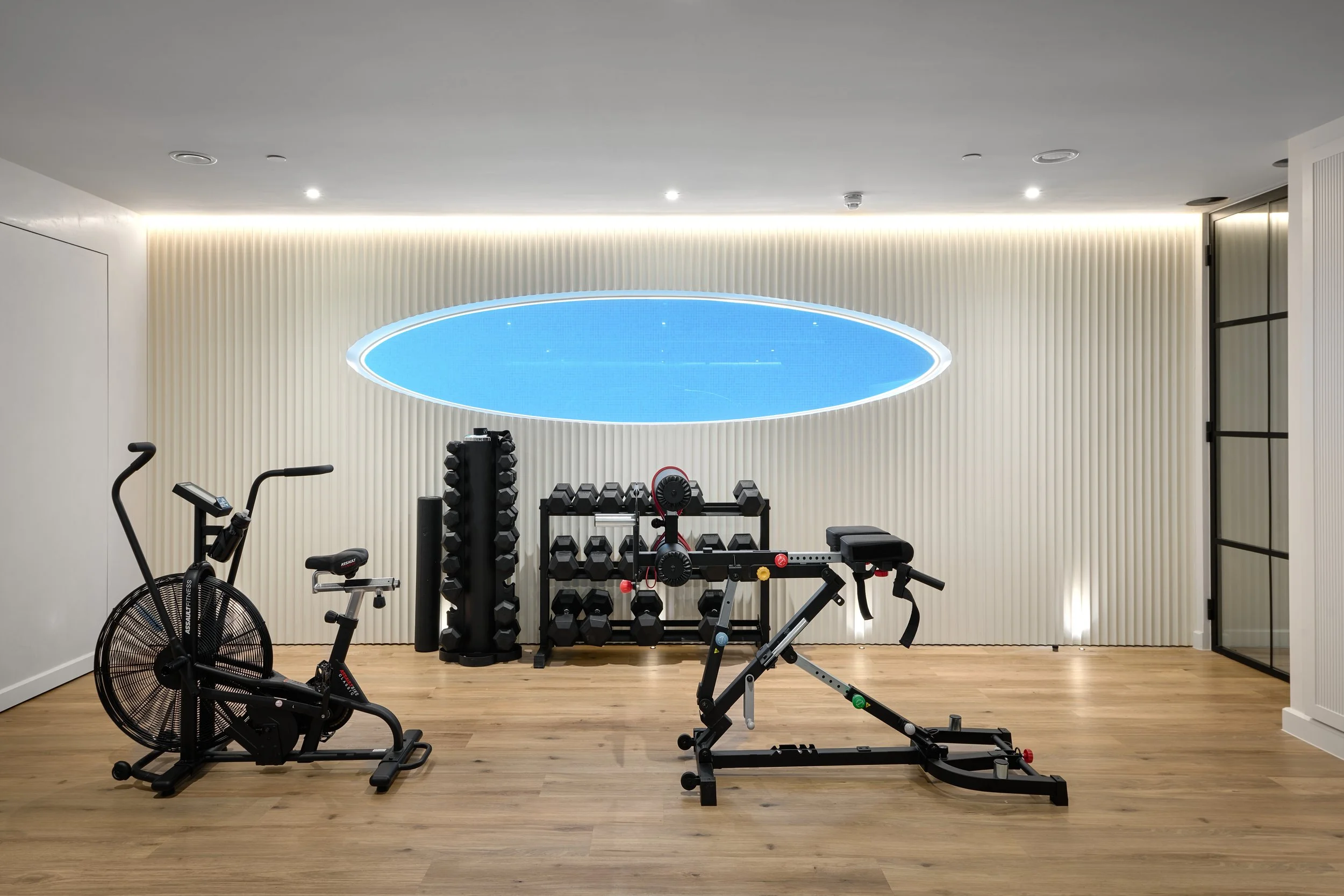 Home gym with exercise bike, adjustable bench, dumbbells, and weights against a wall with a circular blue and white ceiling feature.