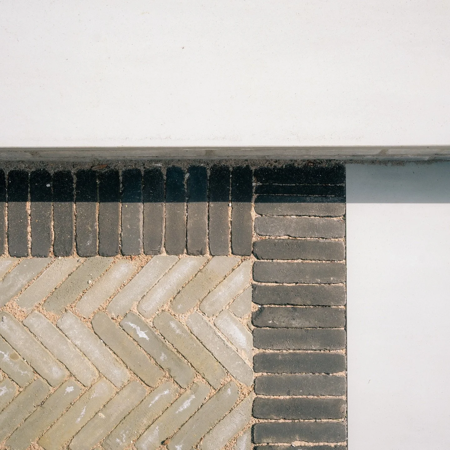Close-up of a corner where a white wall, a concrete band, and a brick pavement meet, showing different pattern and color of the surfaces.