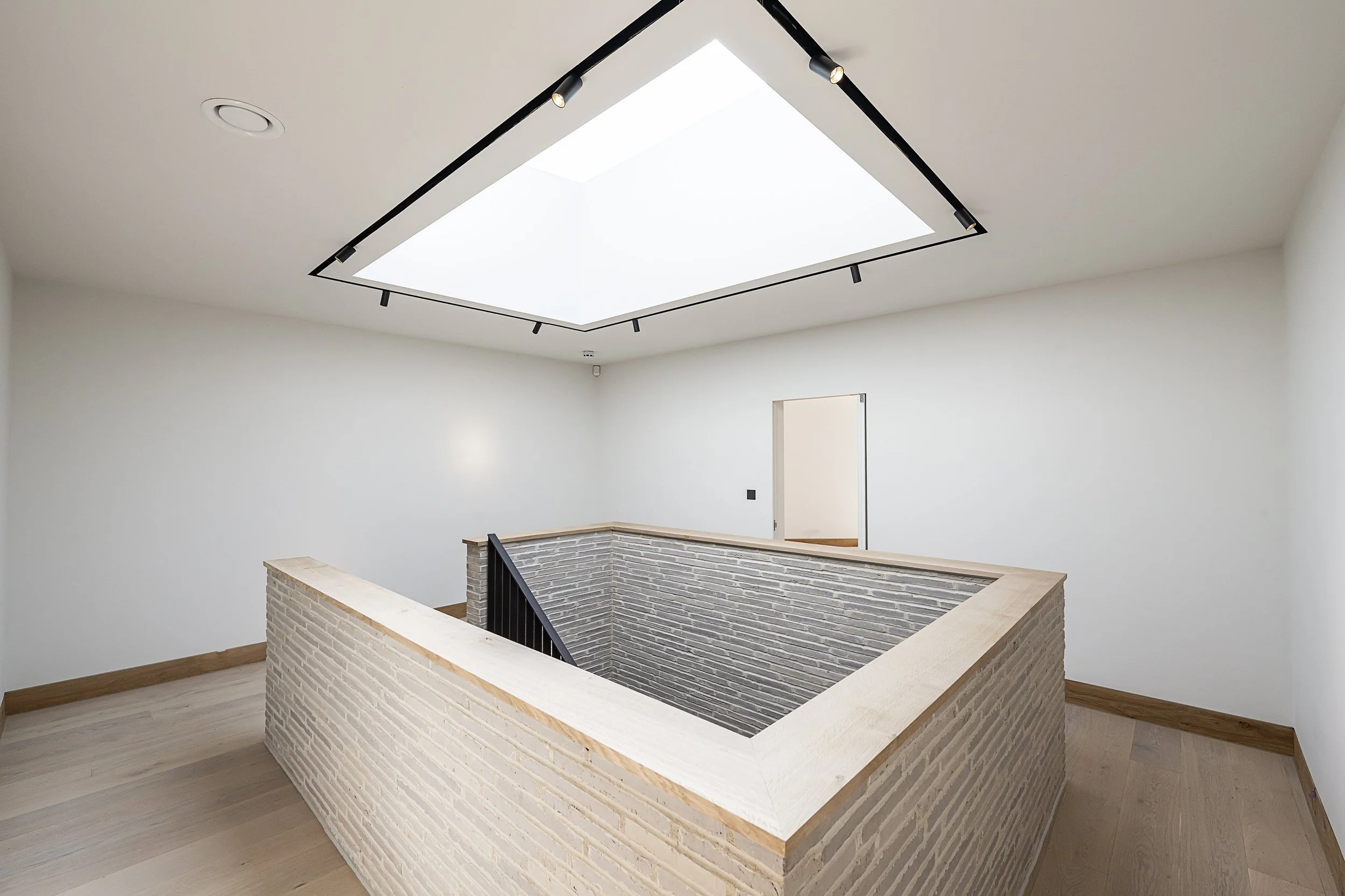 Interior of a modern house with a skylight, white walls, wooden trim, and a brick-lined stairwell.