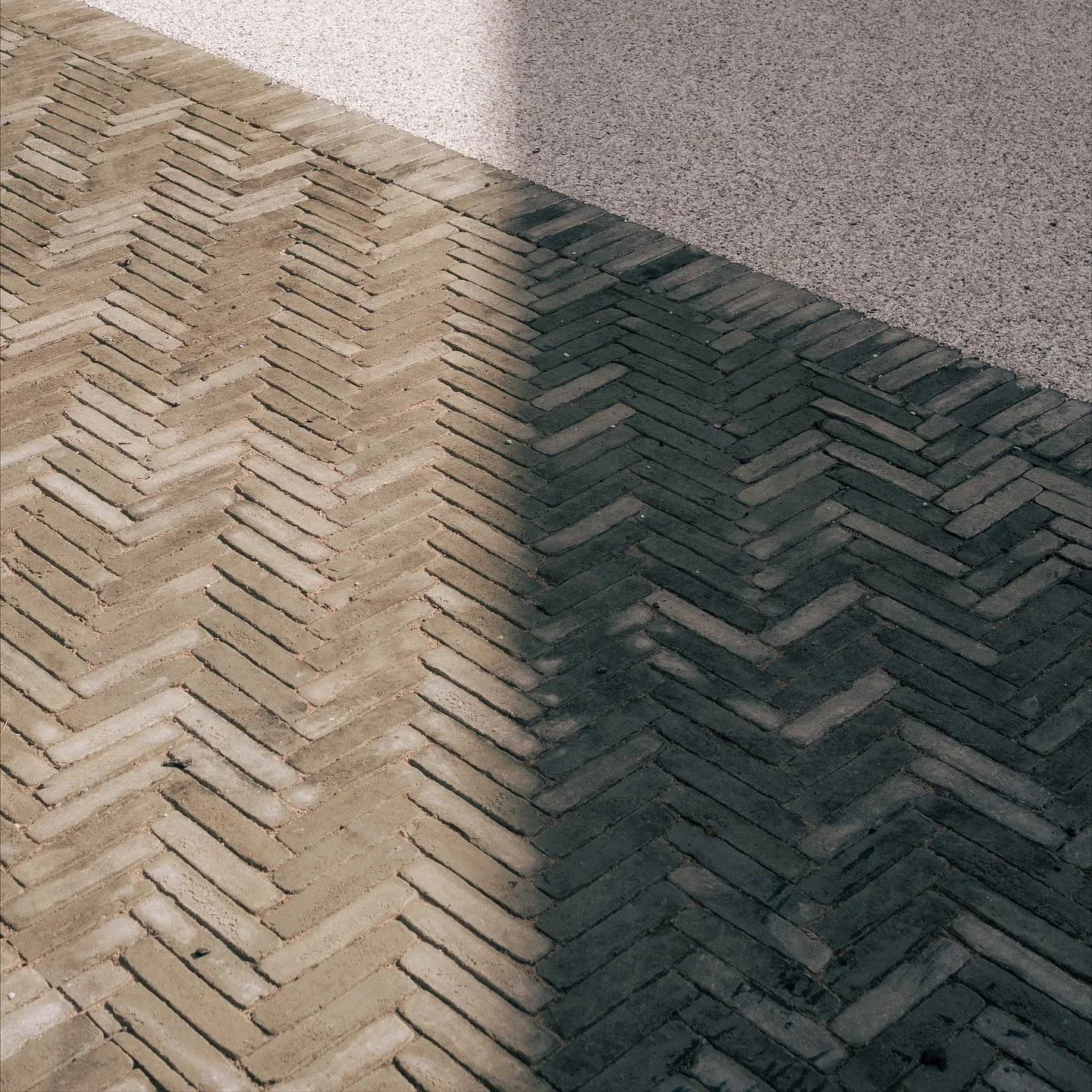 Close-up of a brick and concrete sidewalk, with the shadow of an object cast across the bricks.