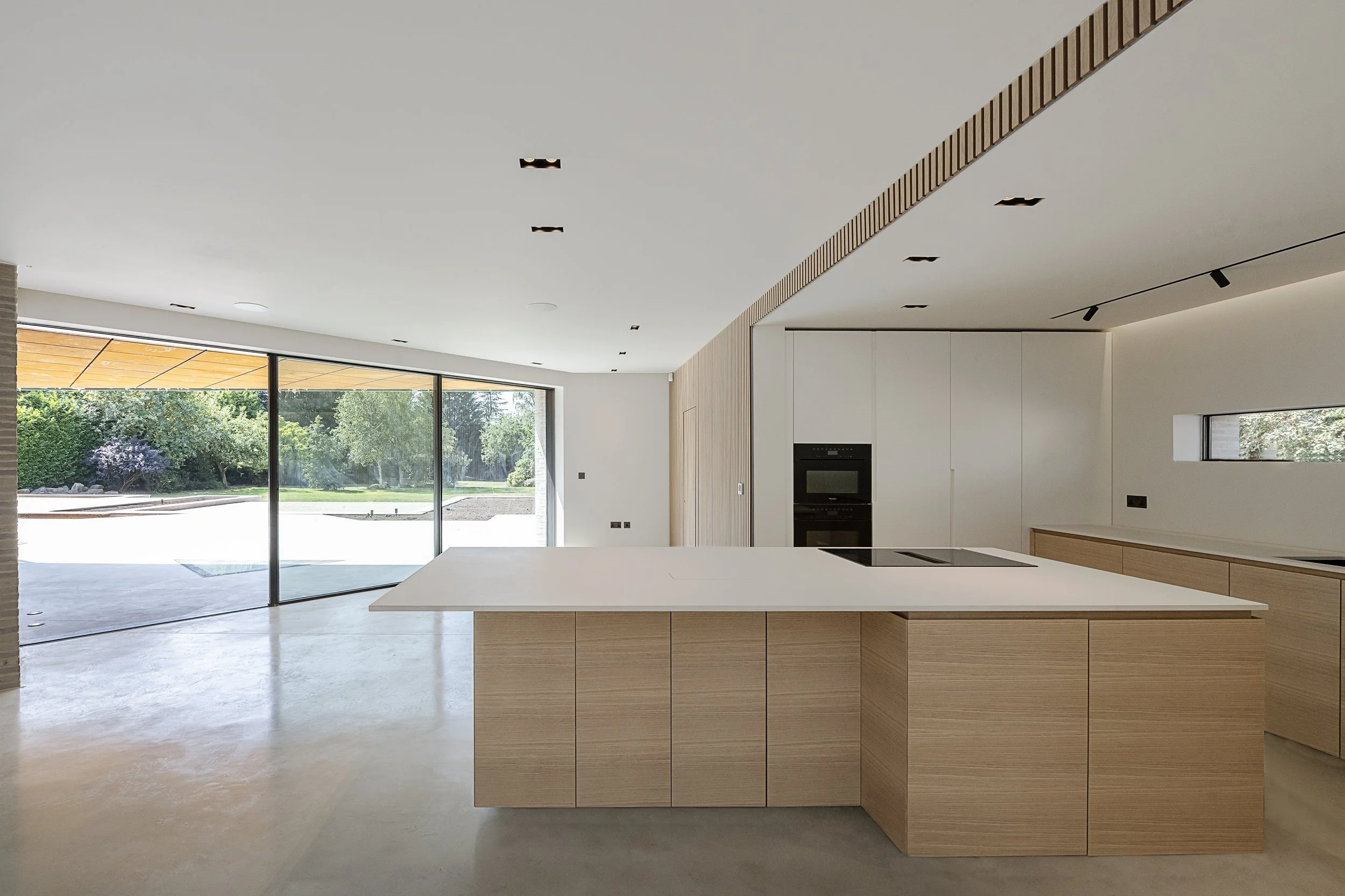Modern kitchen with white island, wooden cabinets, and large sliding glass doors overlooking a green outdoor space.