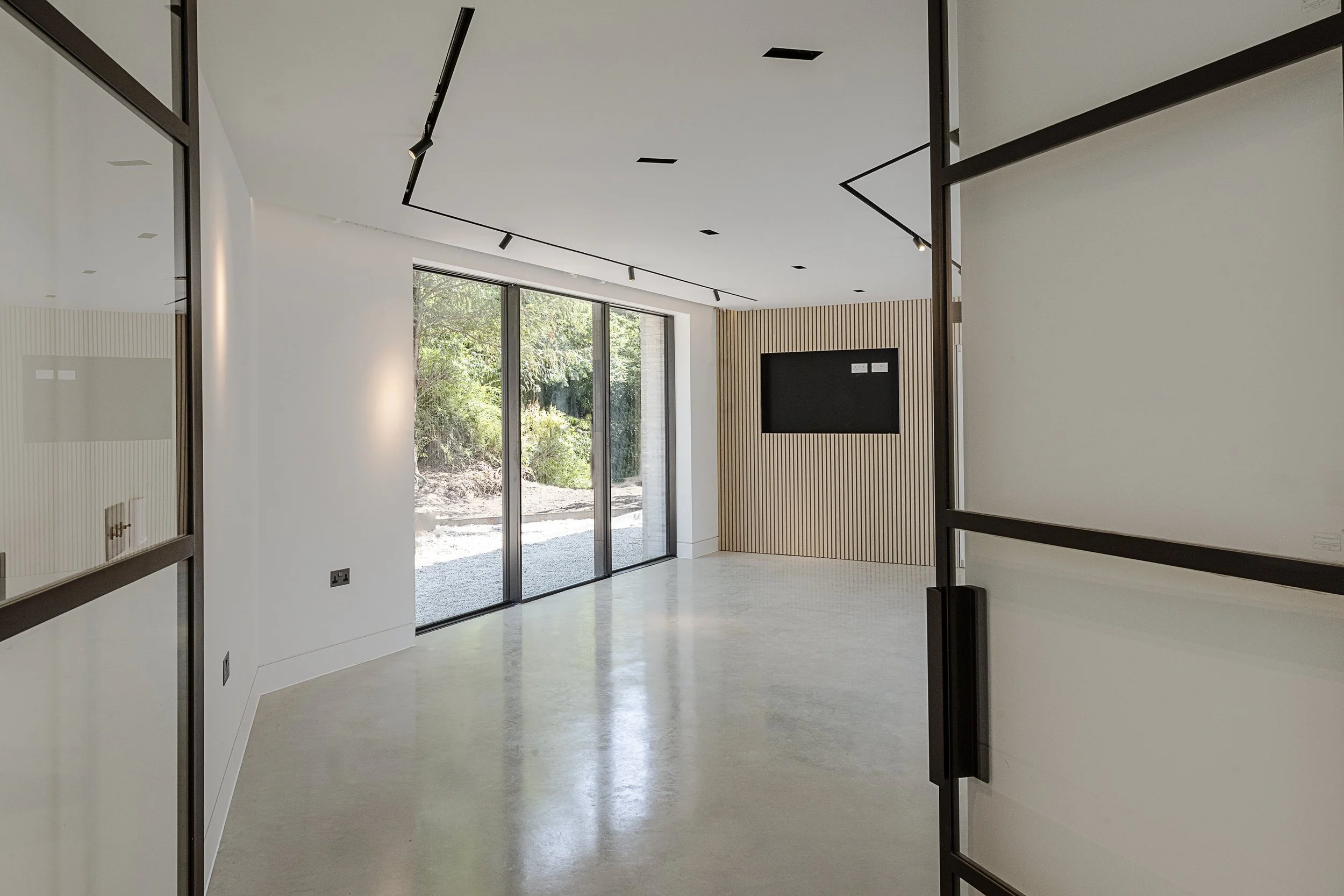 Modern, empty room with large glass sliding doors, wooden wall paneling, and a wall-mounted TV.