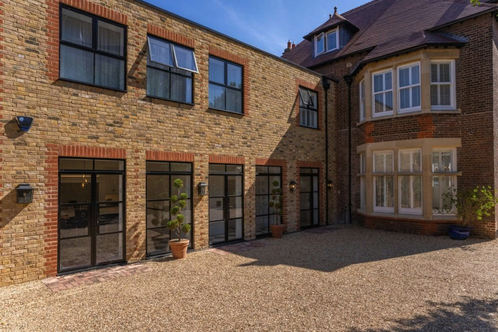 Modern brick building with large glass doors and windows, potted plants, and a gravel courtyard.