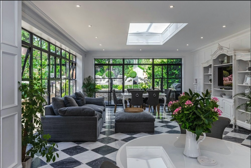 Living room with large windows, gray couches, a round white table with pink flowers, and a black and white checkered floor.