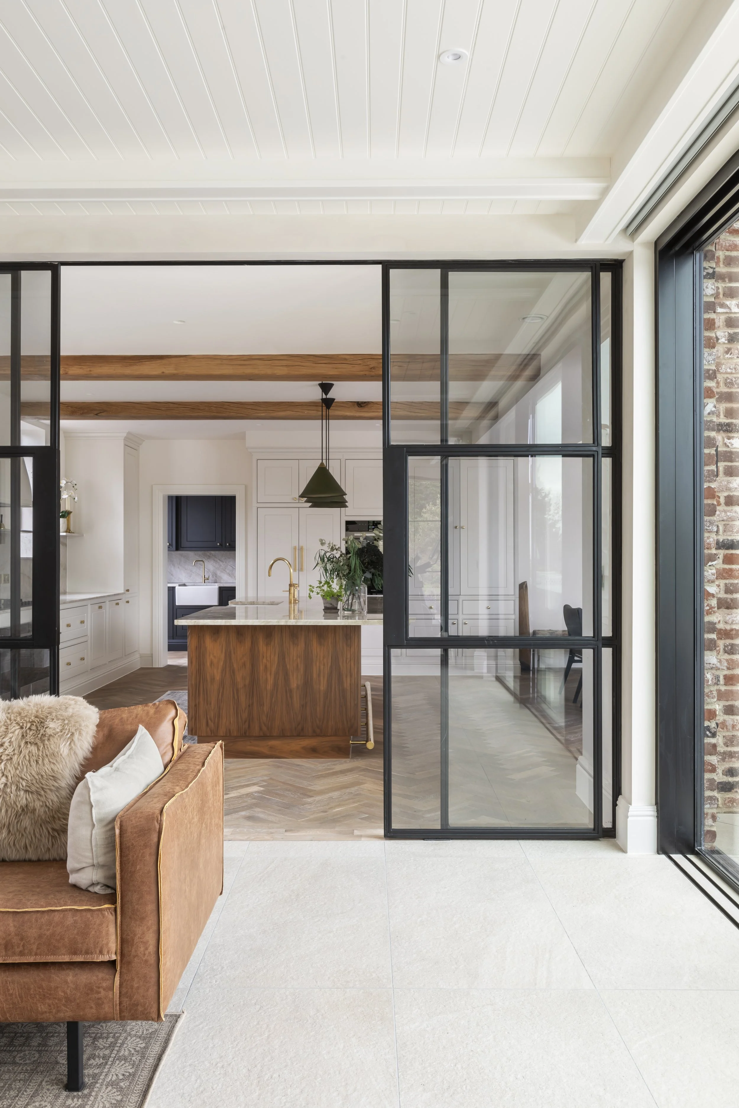 Open-concept kitchen and living area with glass partition, white cabinetry, wooden countertop, and a brown sofa with a furry pillow.