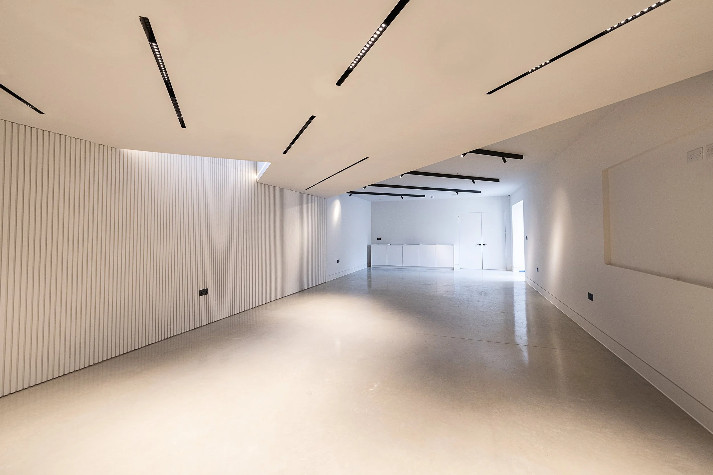 Empty modern room with white walls, a textured white wall on the left, and black ceiling light fixtures.