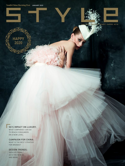 Fashion magazine cover featuring a woman in a light pink feathered dress and white tulle skirt with a feathered hat, set against a dark background.